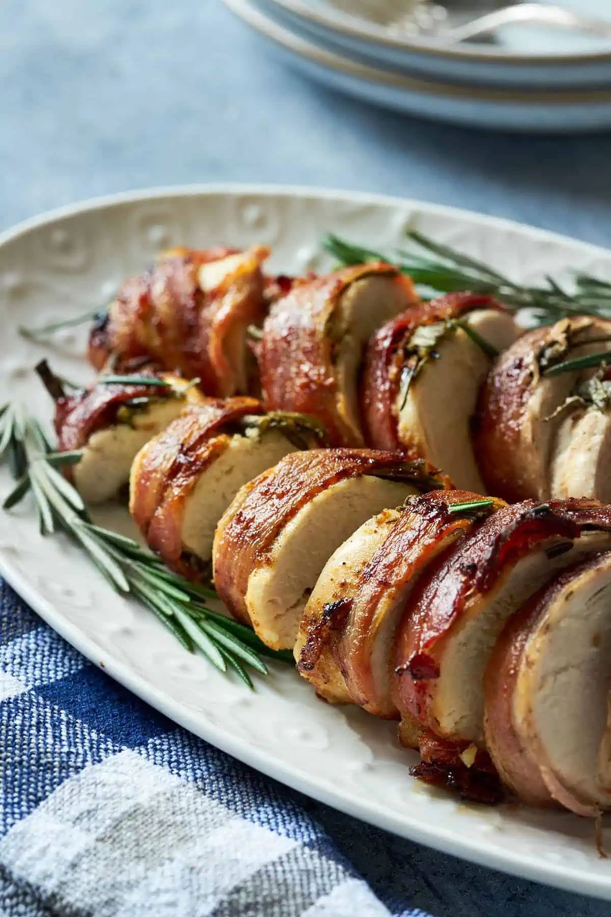 Air fryer bacon-wrapped chicken breast served on a plate and garnished with rosemary. 