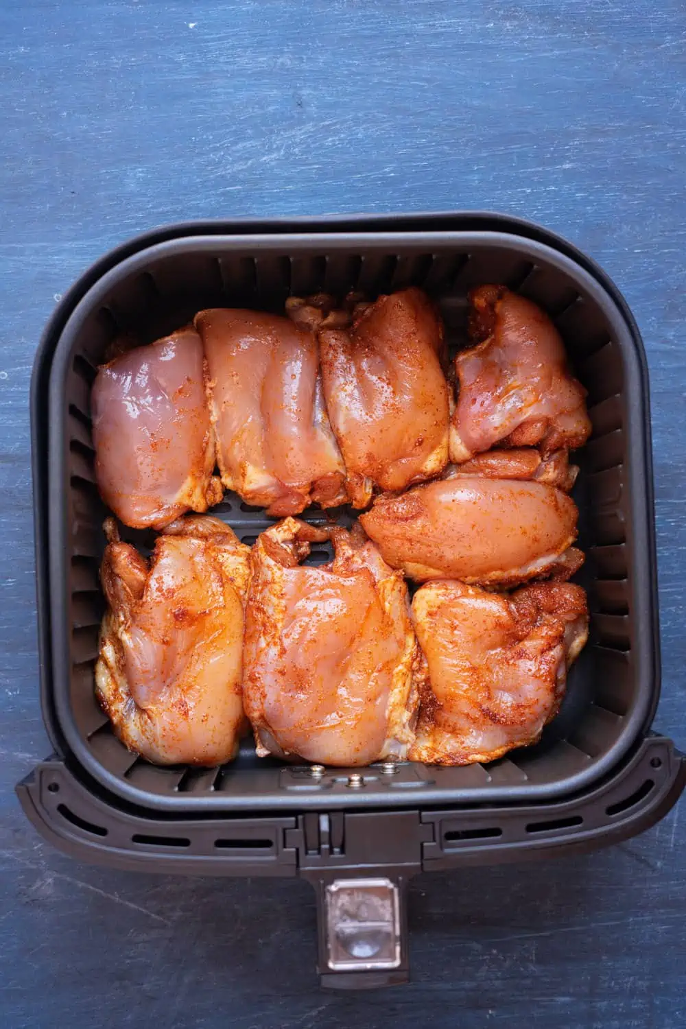 Seasoned chicken thighs in the air fryer basket.