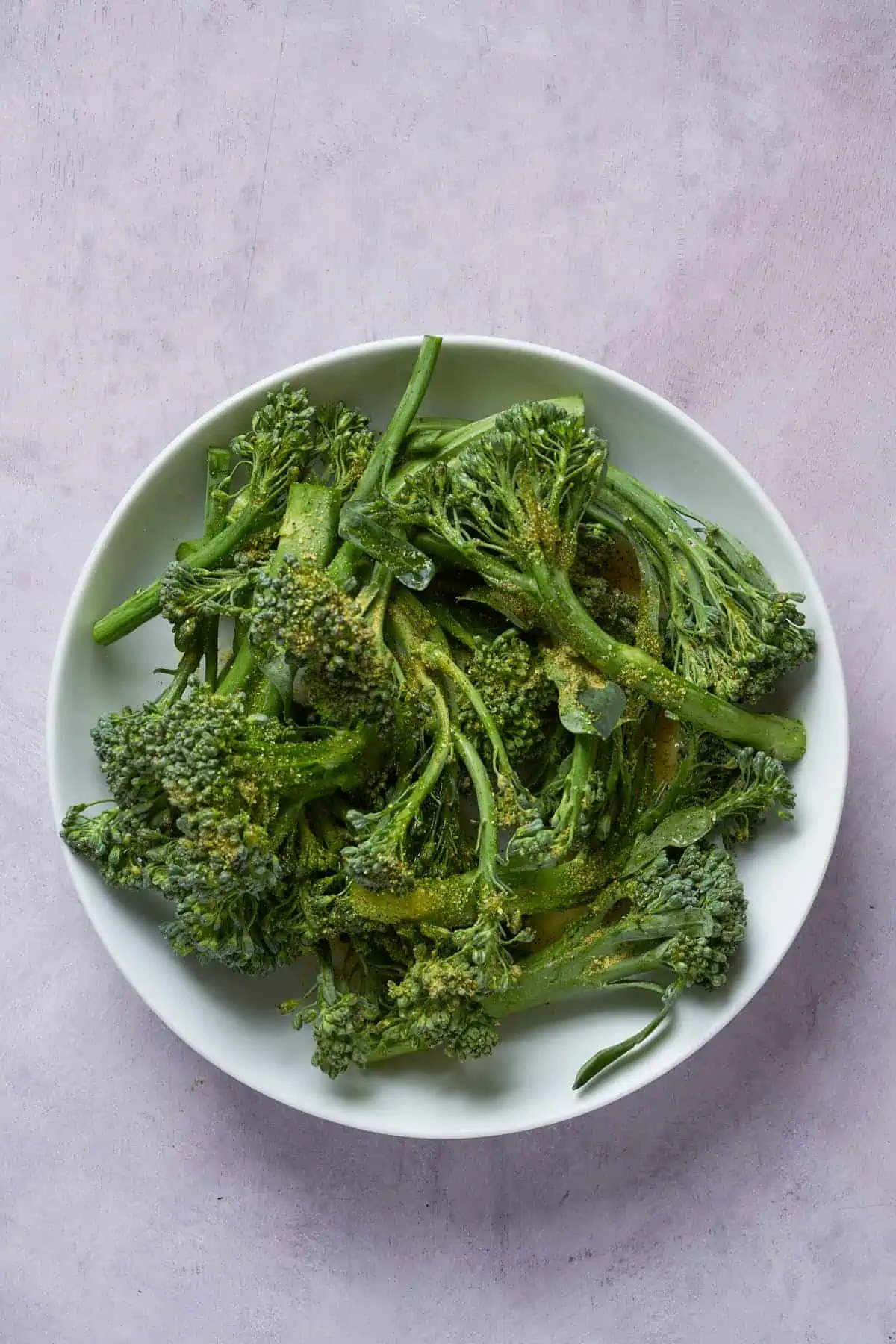 Broccolini in a bowl with olive oil and seasoning.