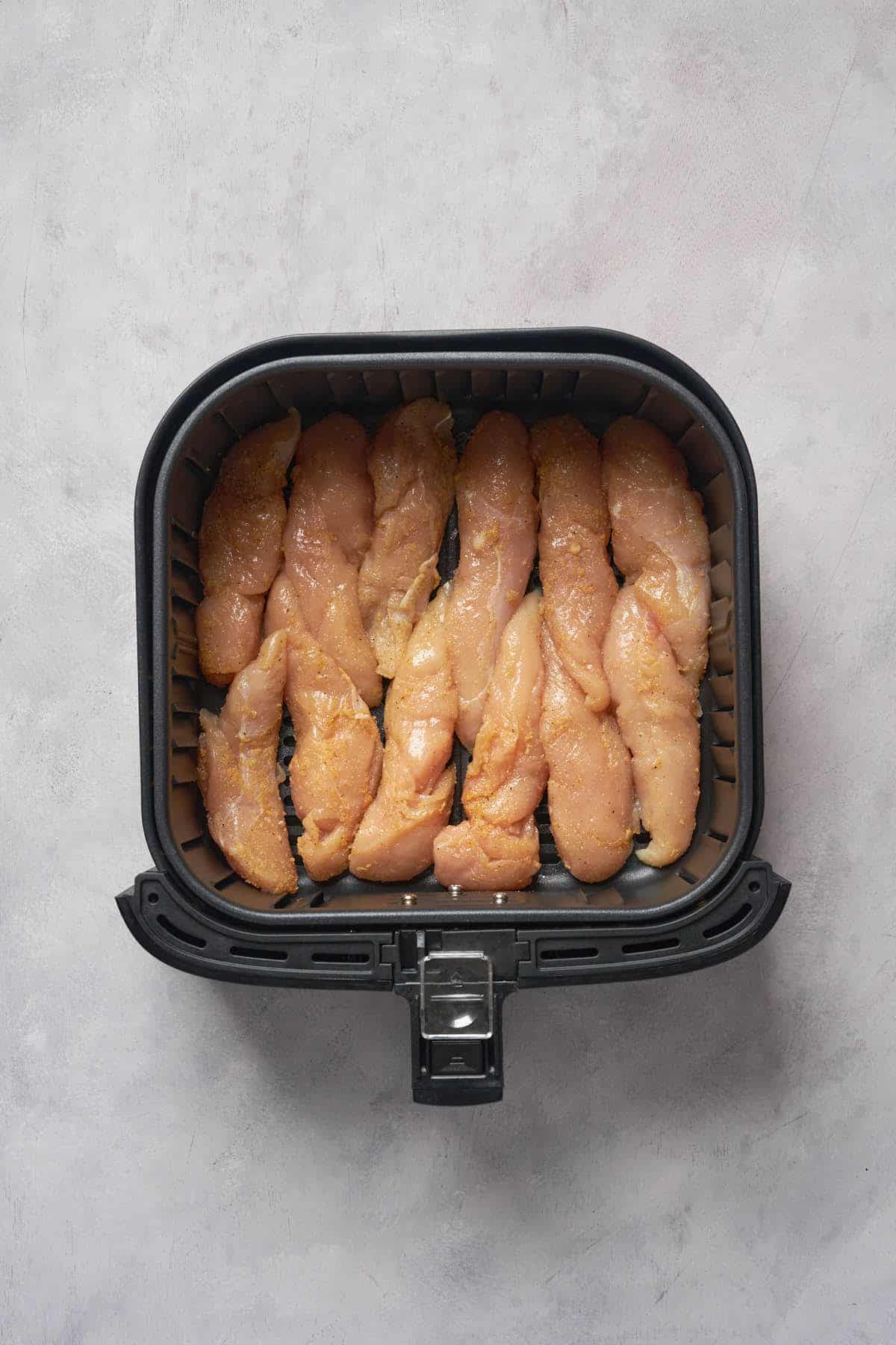 Uncooked chicken tenders in the air fryer basket.