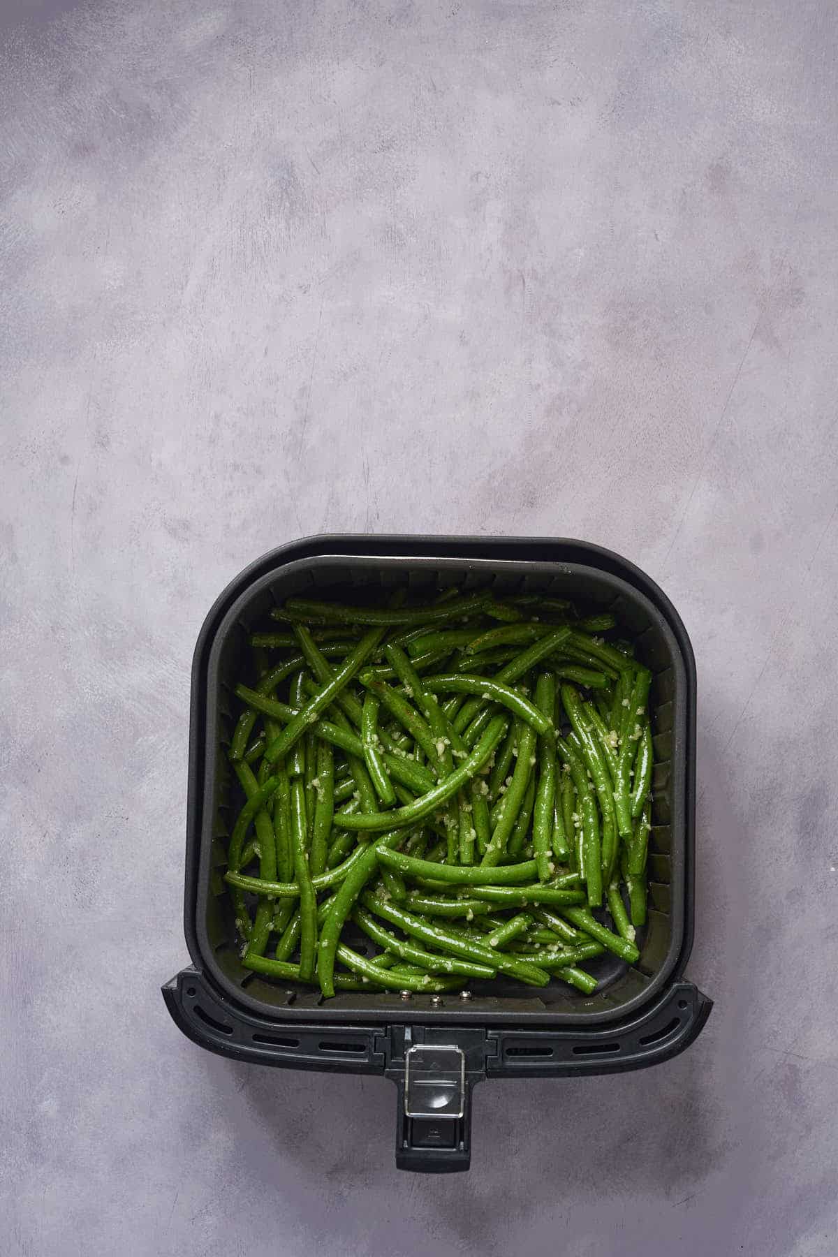 Uncooked garlic green beans in the air fryer basket.