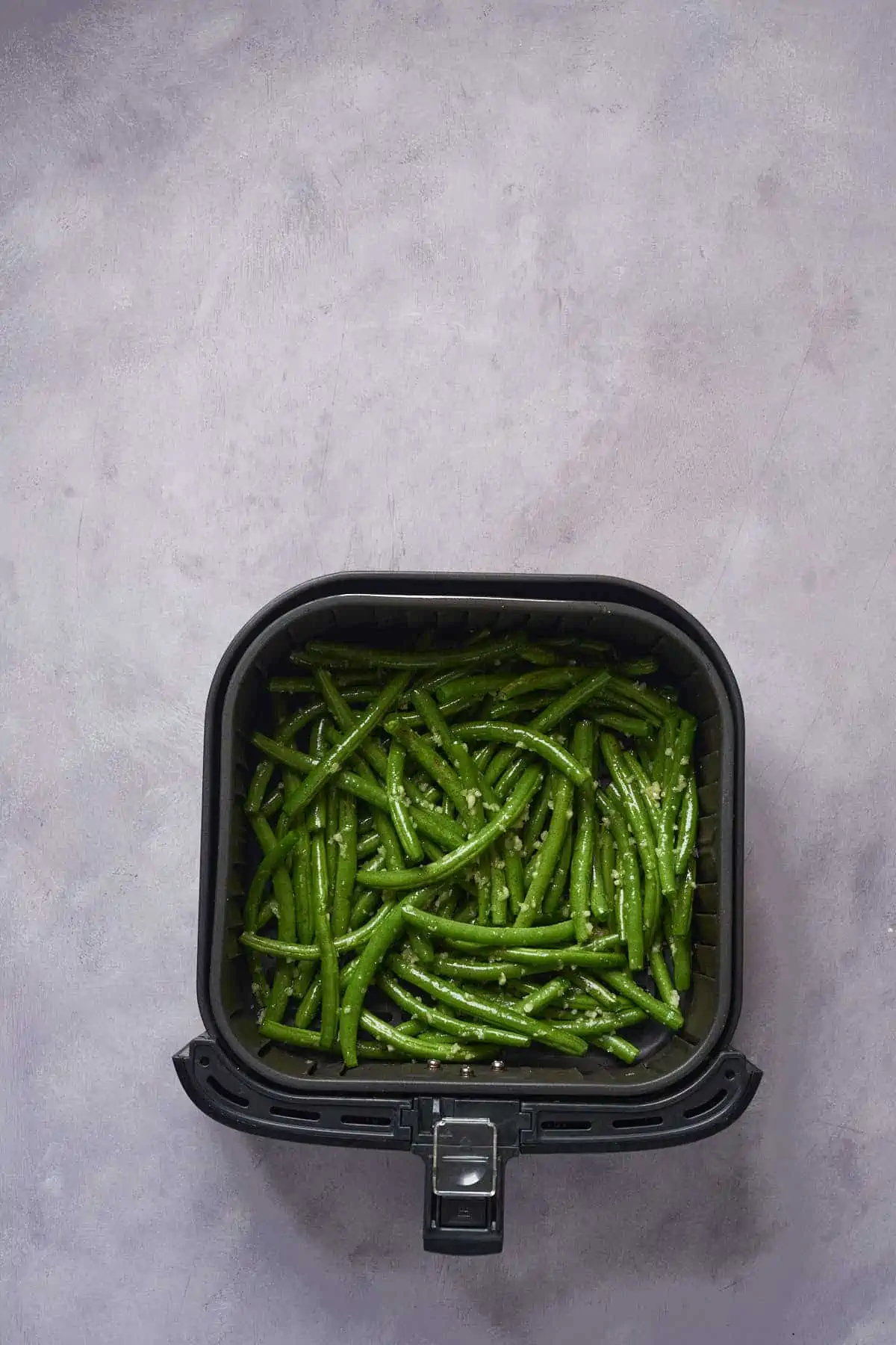 Uncooked garlic green beans in the air fryer basket.