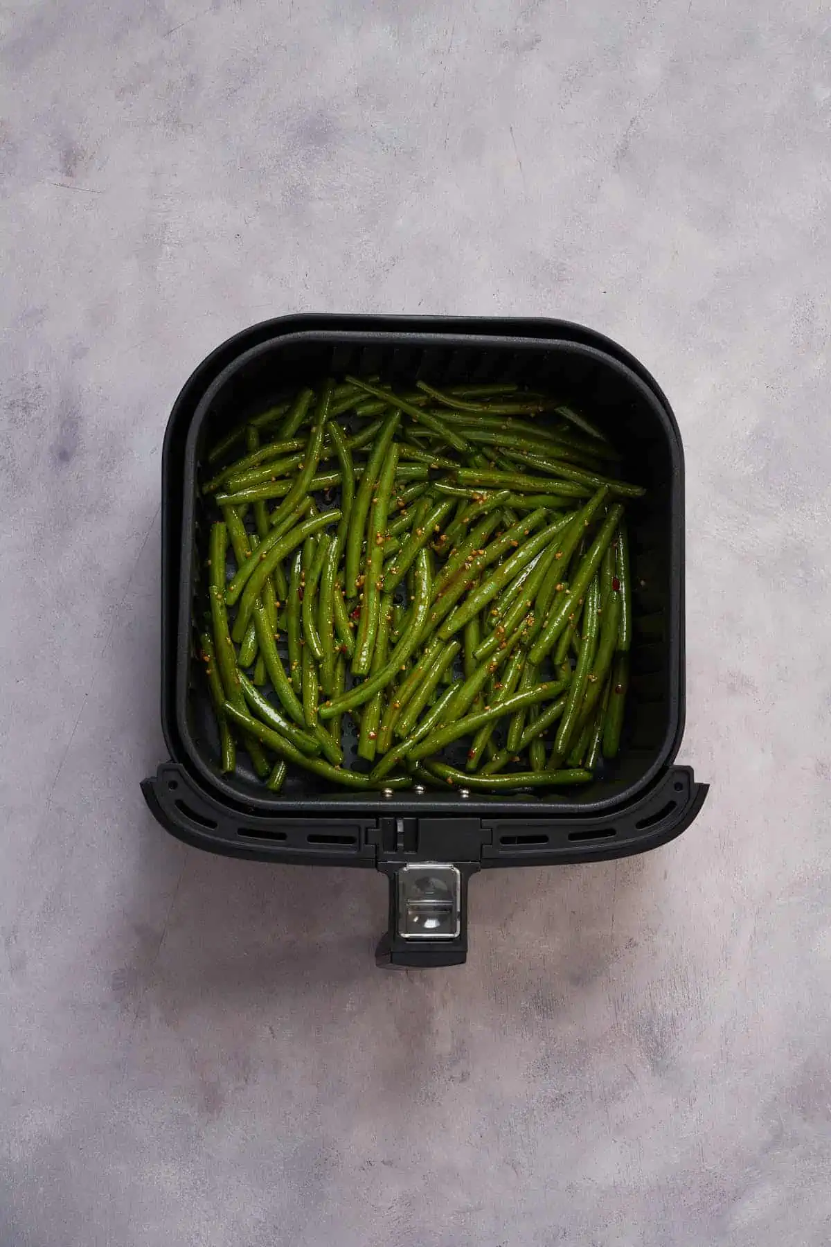 Green beans in the air fryer basket before cooking with spicy sauce.