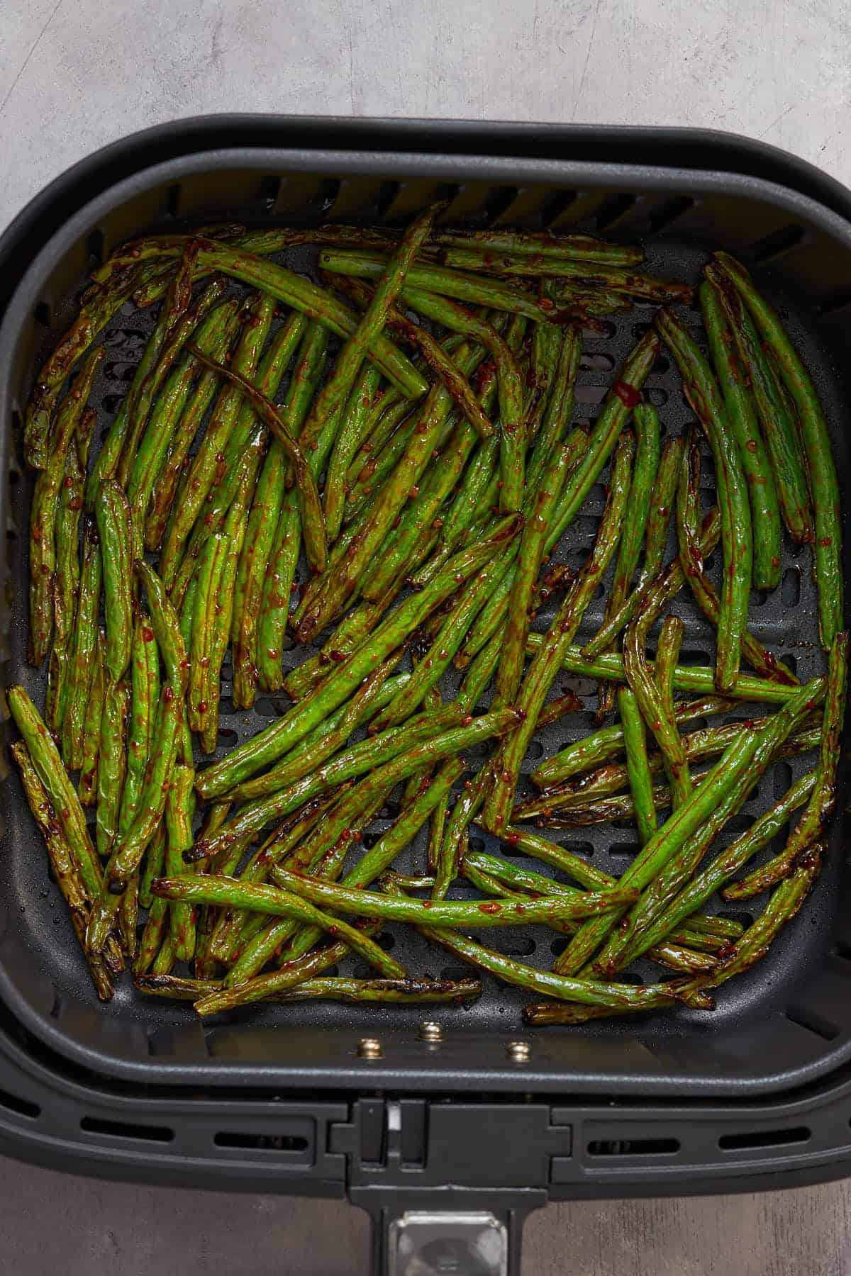 Air fried spicy green beens in the air fryer basket.