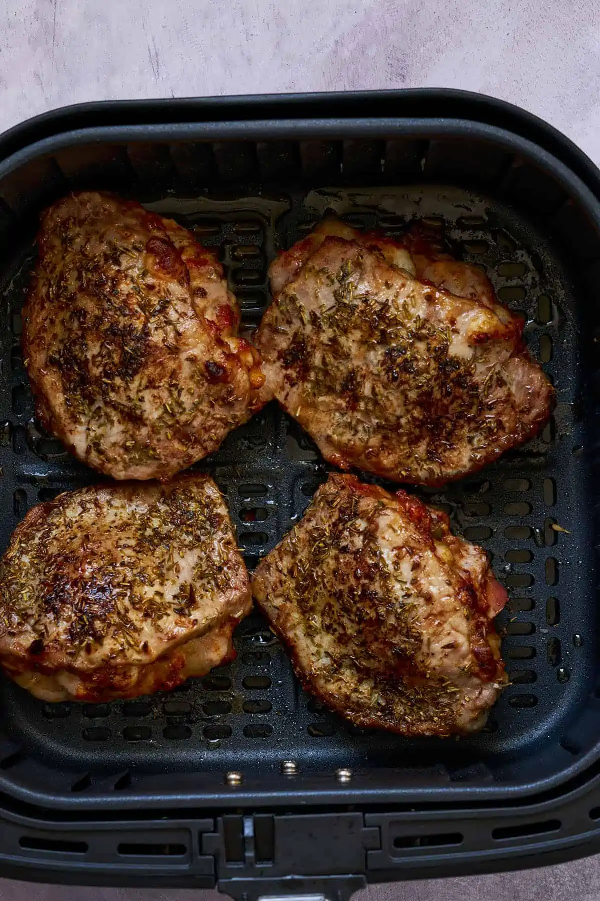 Stuffed pork chops seasoned with oregano, rosemary, and thyme in the air fryer basket.