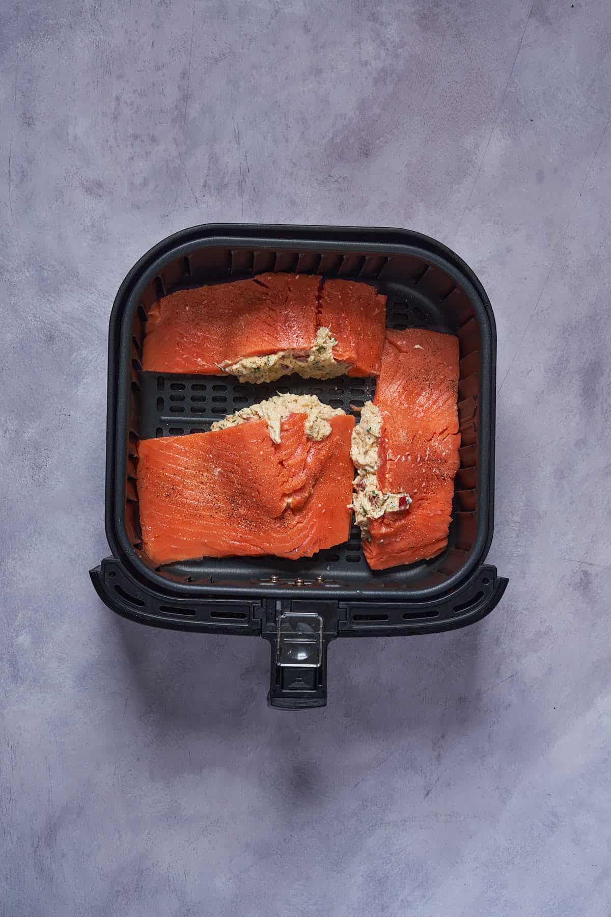 Salmon fillets stuffed with the crab meat mixture in the air fryer basket before cooking.