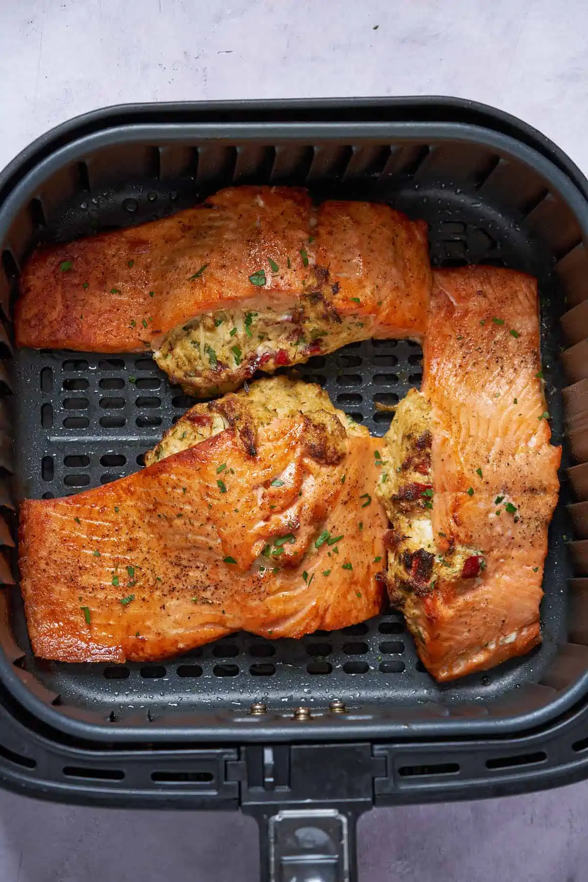 Stuffed salmon in air fryer sprinkled with fresh herbs.