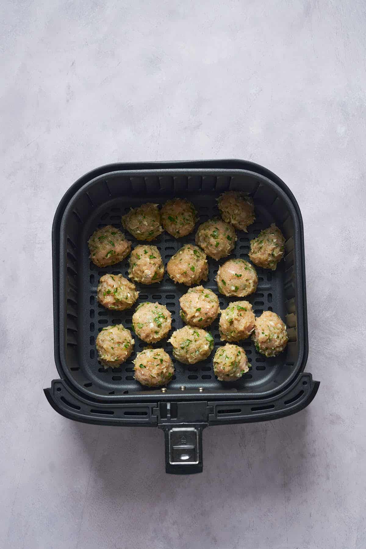 Uncooked turkey meatballs in the air fryer basket.