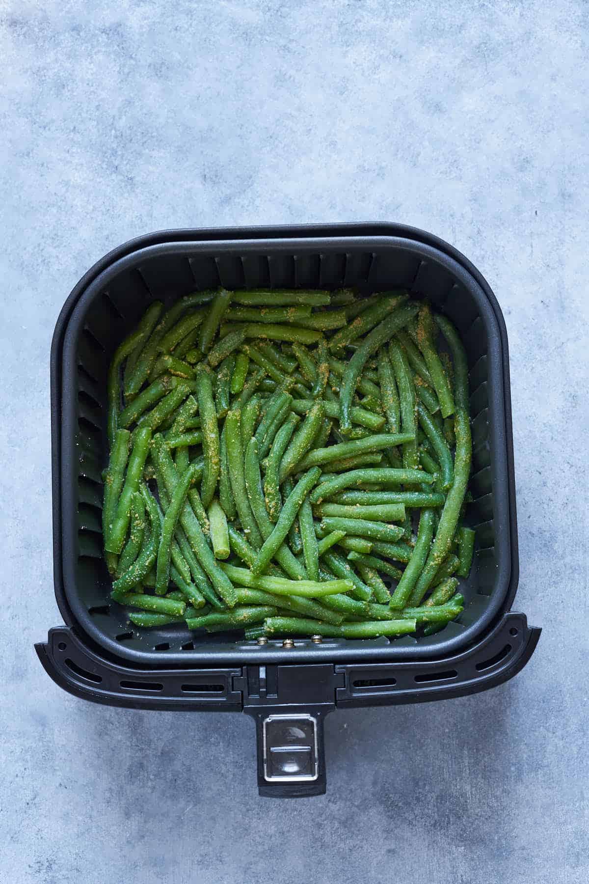 Seasoned frozen green beans in the air fryer basket.