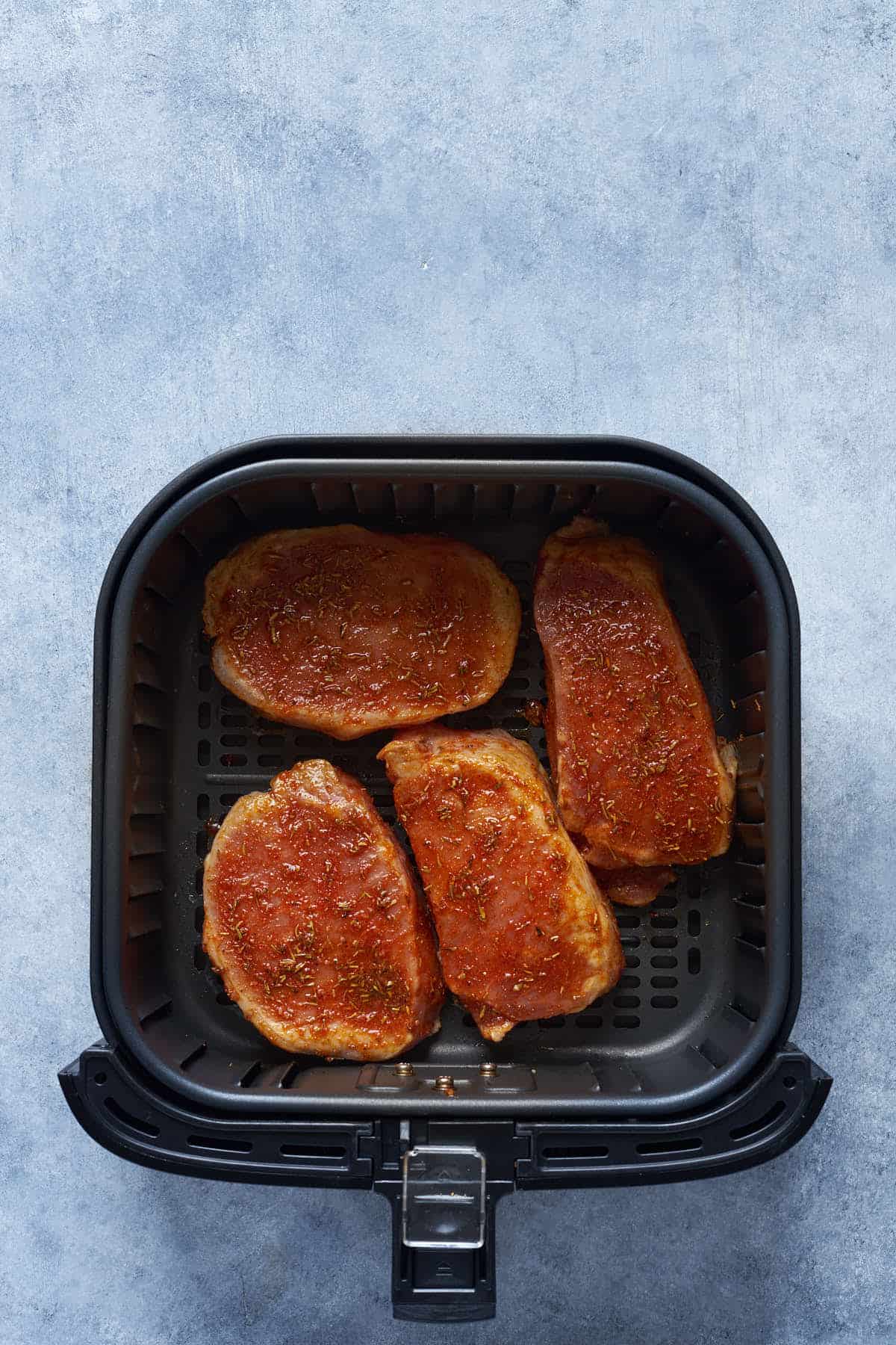Pork chops brushed with oil mixture in the air fryer basket.