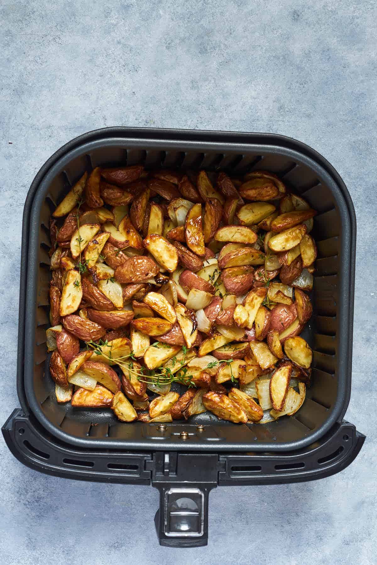 Air fried potatoes and onion in the air fryer basket.