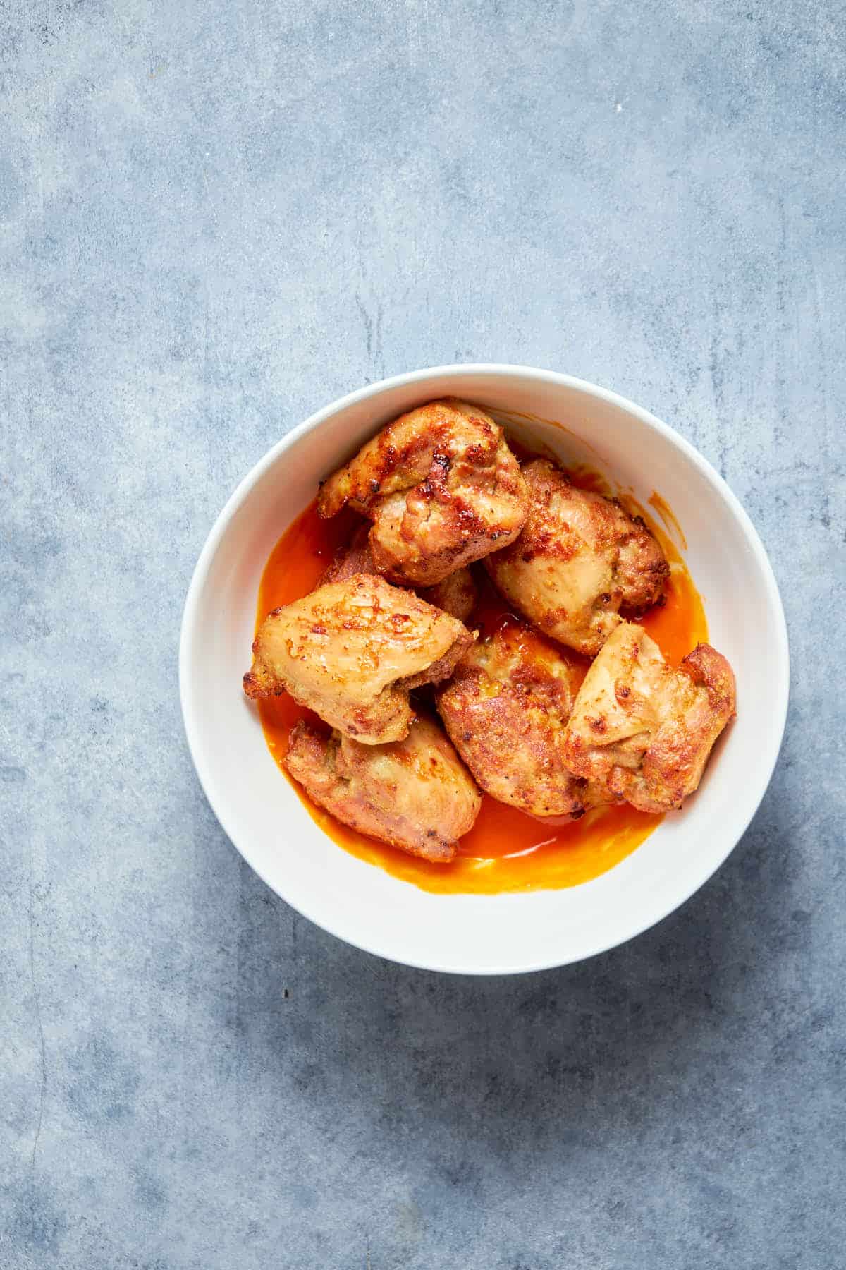 Coating the cooked chicken thighs with buffalo sauce in a bowl.