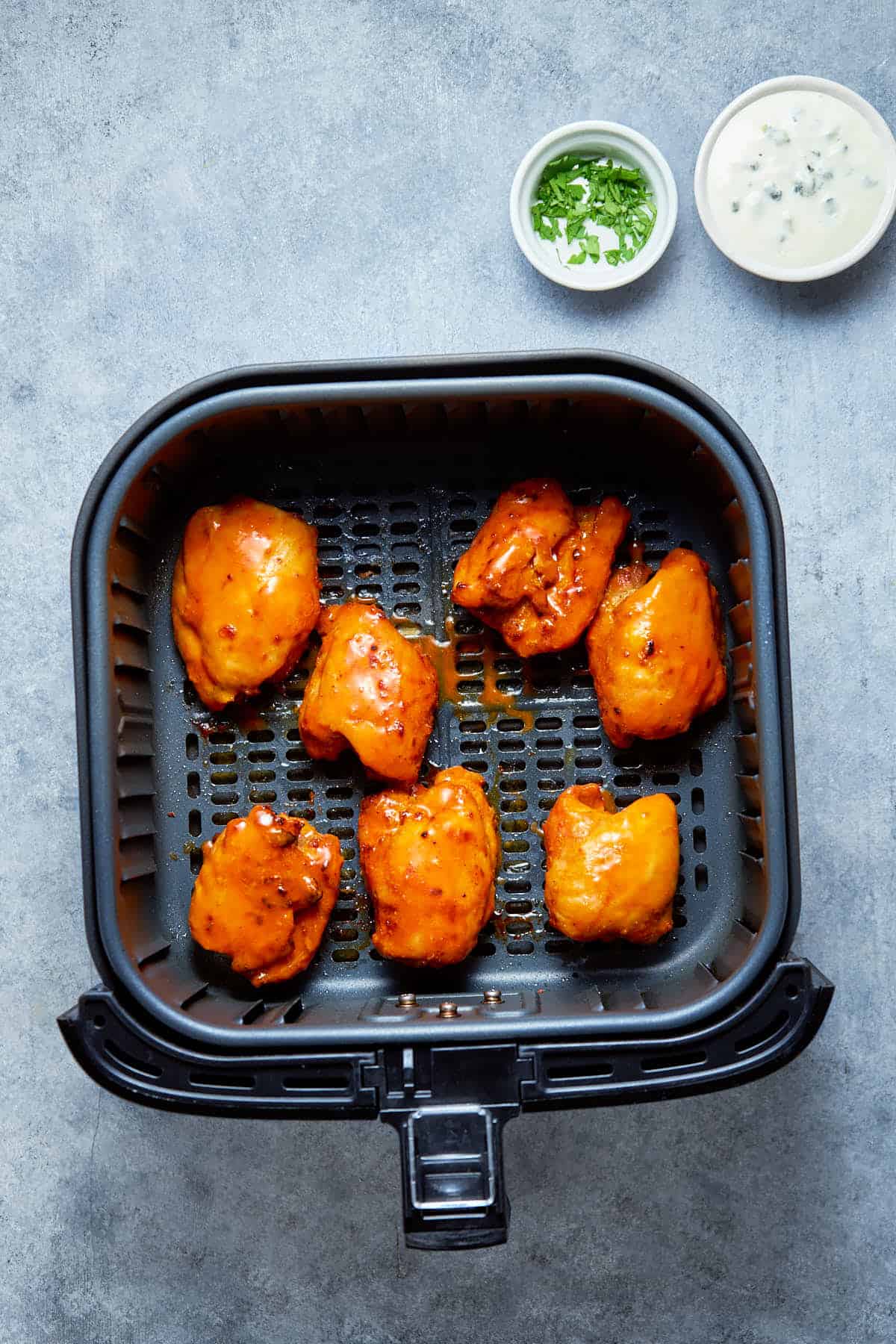 air-fried buffalo chicken thighs in the air fryer basket after cooking.