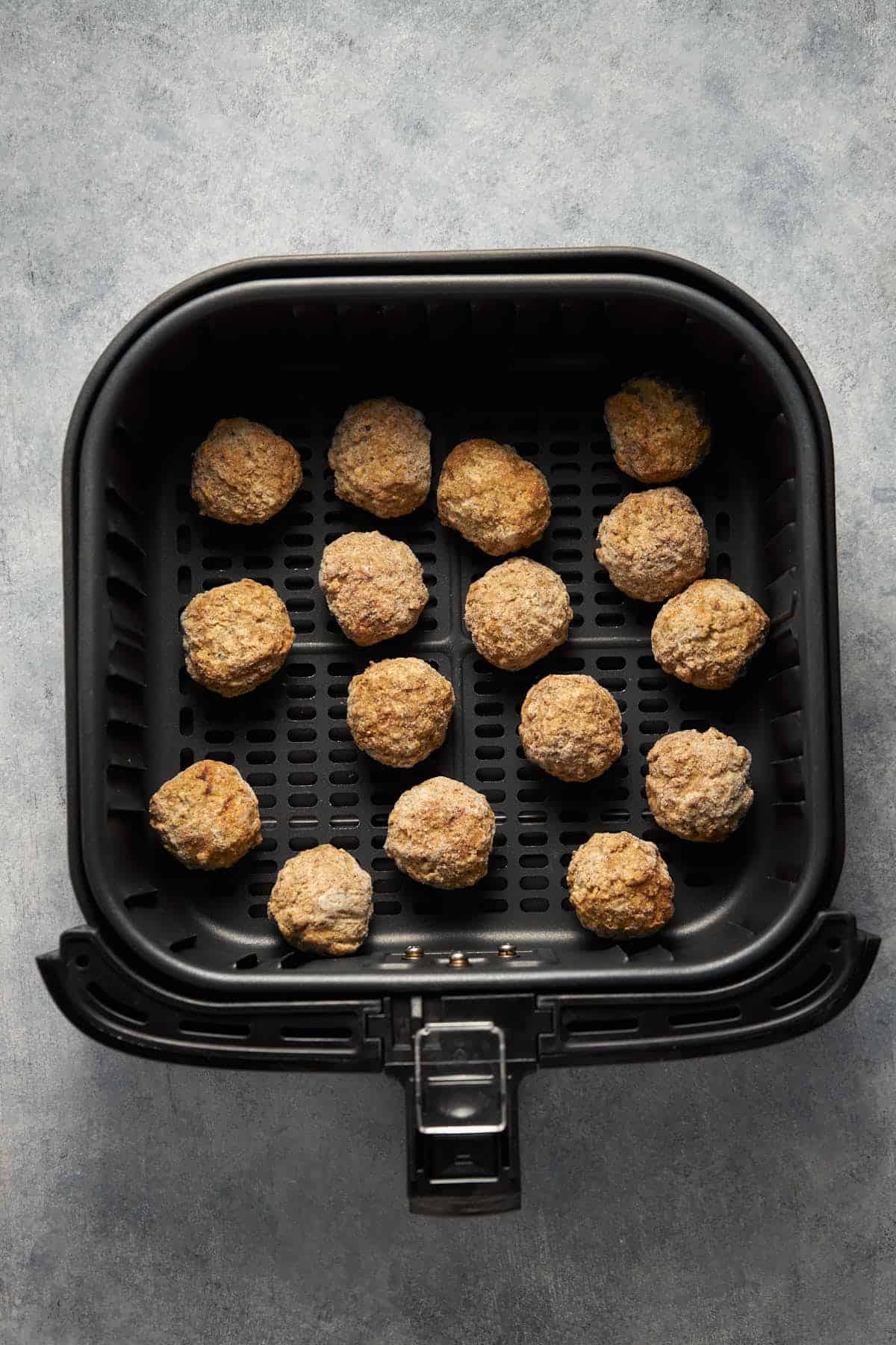 Frozen meatballs in the air fryer basket before cooking.