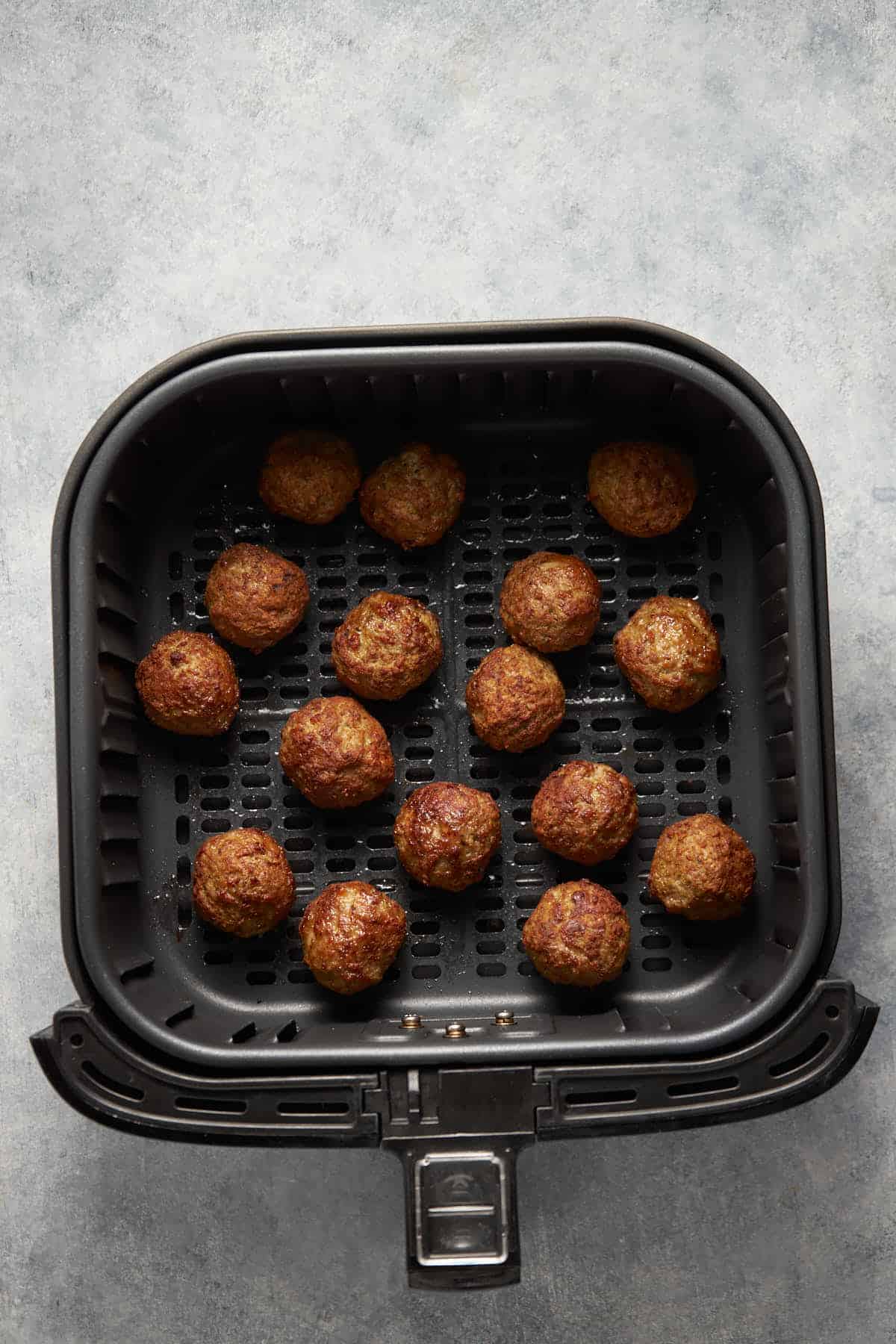 The frozen meatballs in an air fryer basket after cooking.