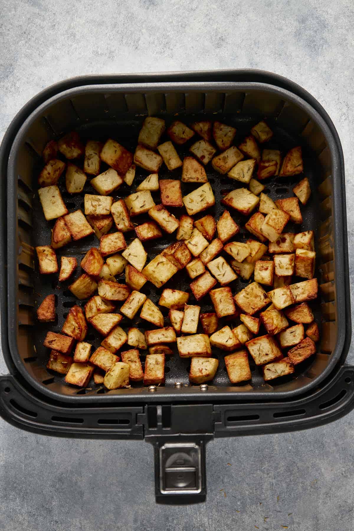 Crispy potato cubes in the air fryer basket after cooking.
