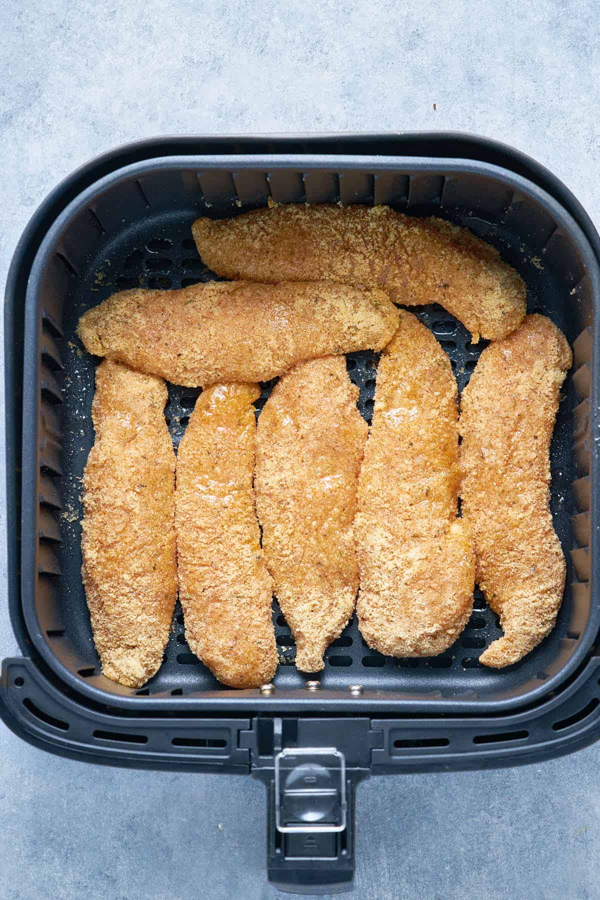 Coated in almond flour with spices, the chicken tenders inside the air fryer before cooking.