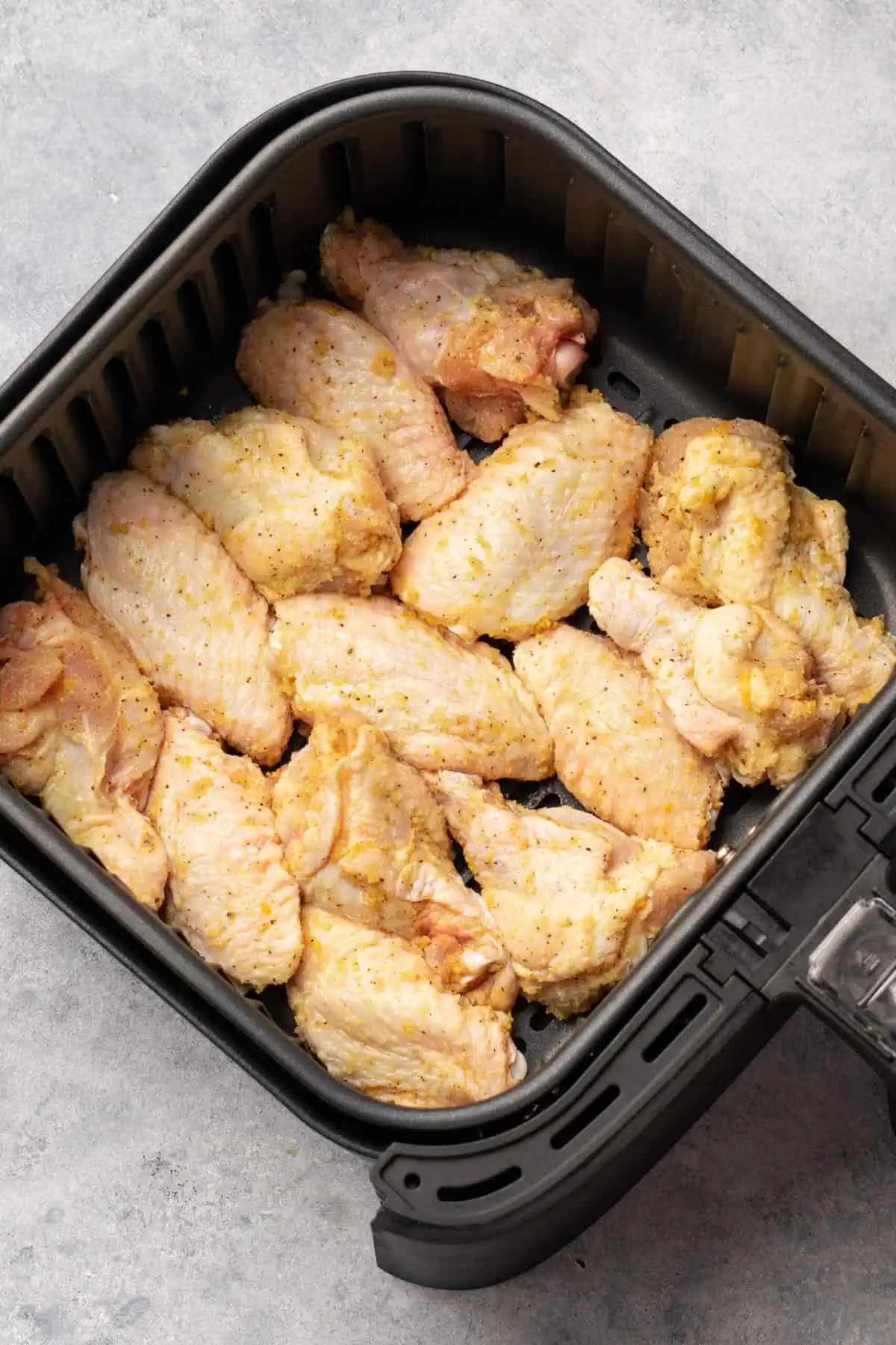 Lemon pepper chicken wings inside the air fryer basket before cooking.
