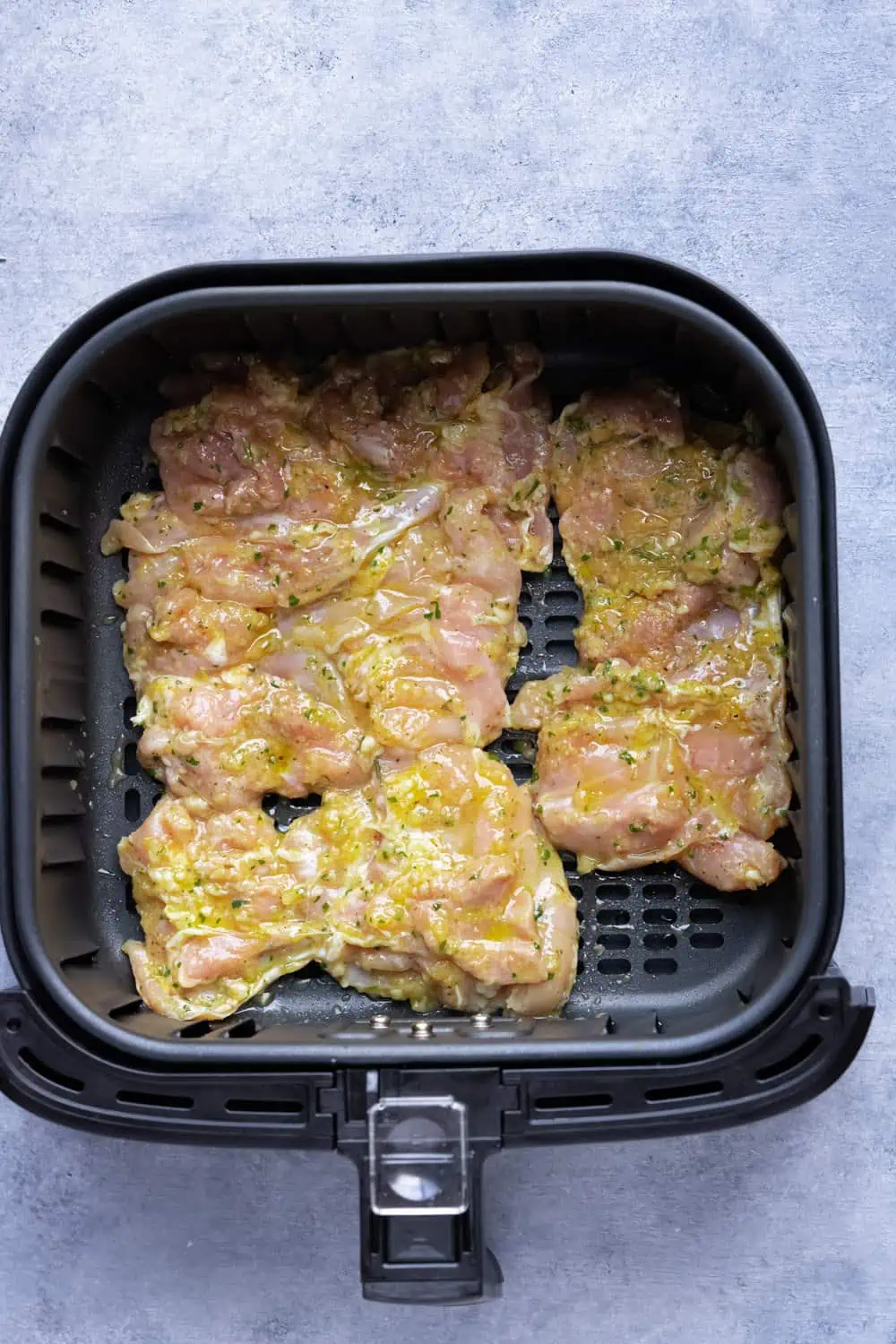 Marinated chicken thighs in the air fryer basket before cooking.