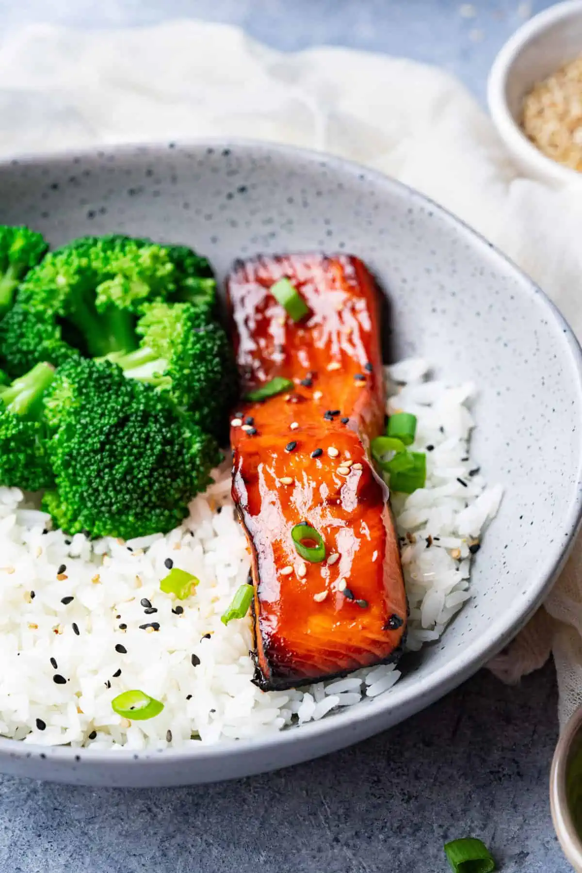 Teriyaki salmon serve with rice, and broccoli and garnished with sesame seeds and green onion.