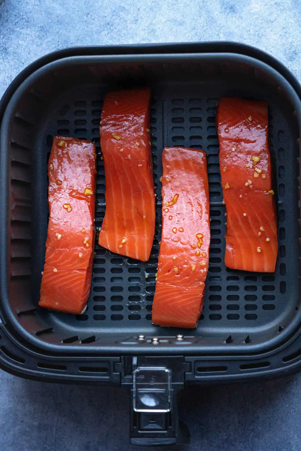 Teriyaki salmon inside the air fryer basket before air frying.