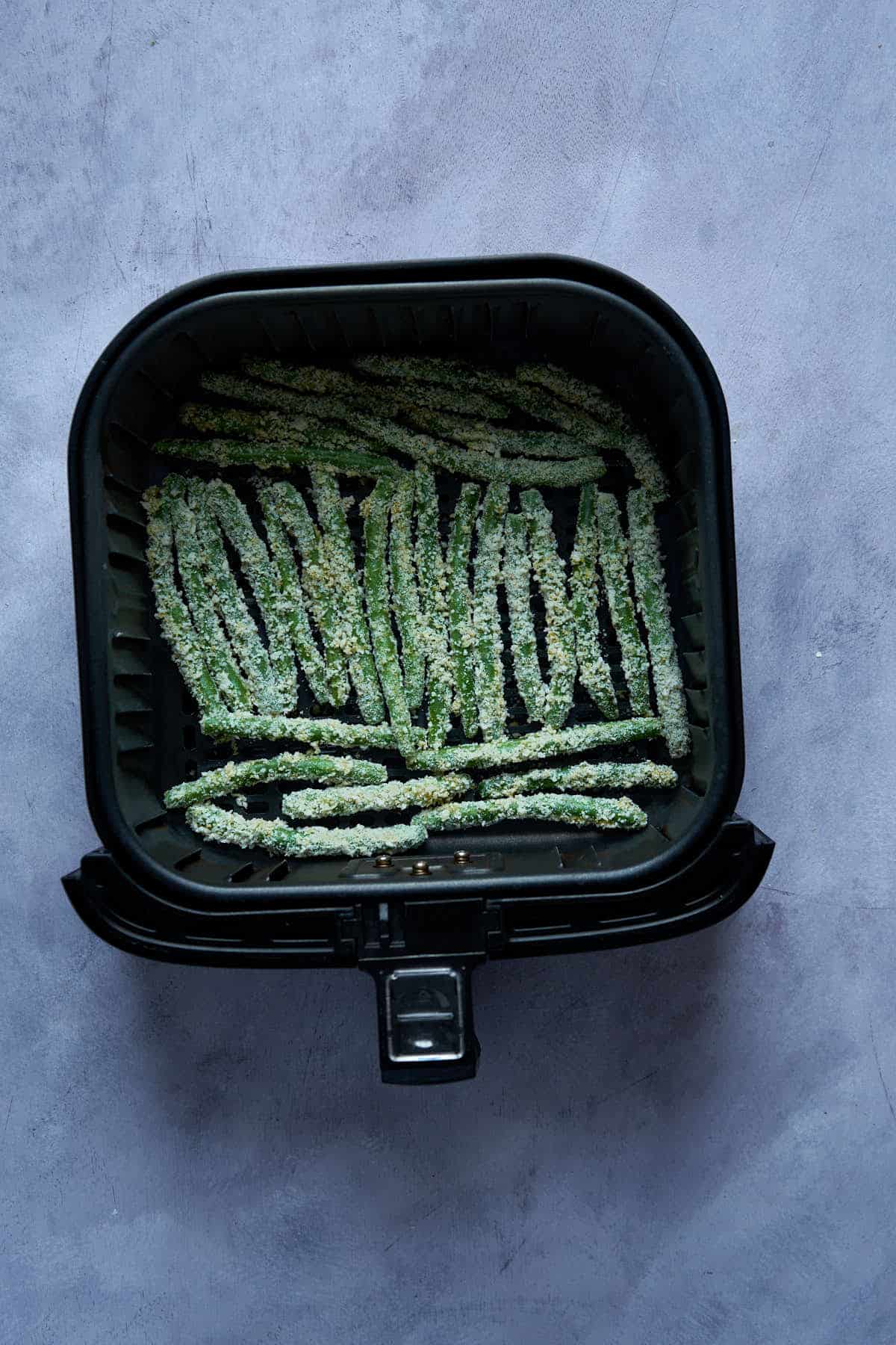 The green beans fries in the air fryer basket before air frying.