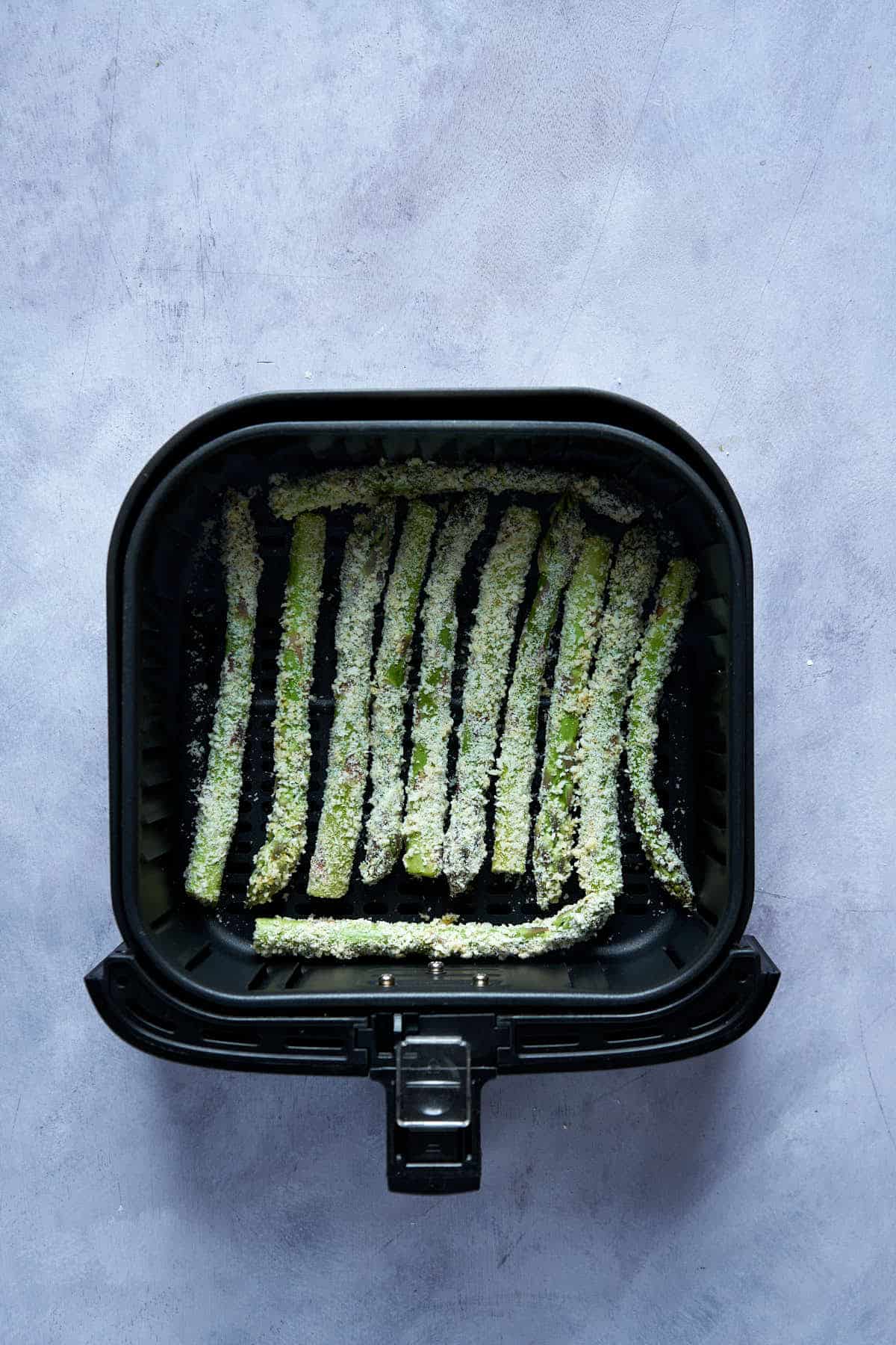 Asparagus fries in the air fryer basket before cooking.