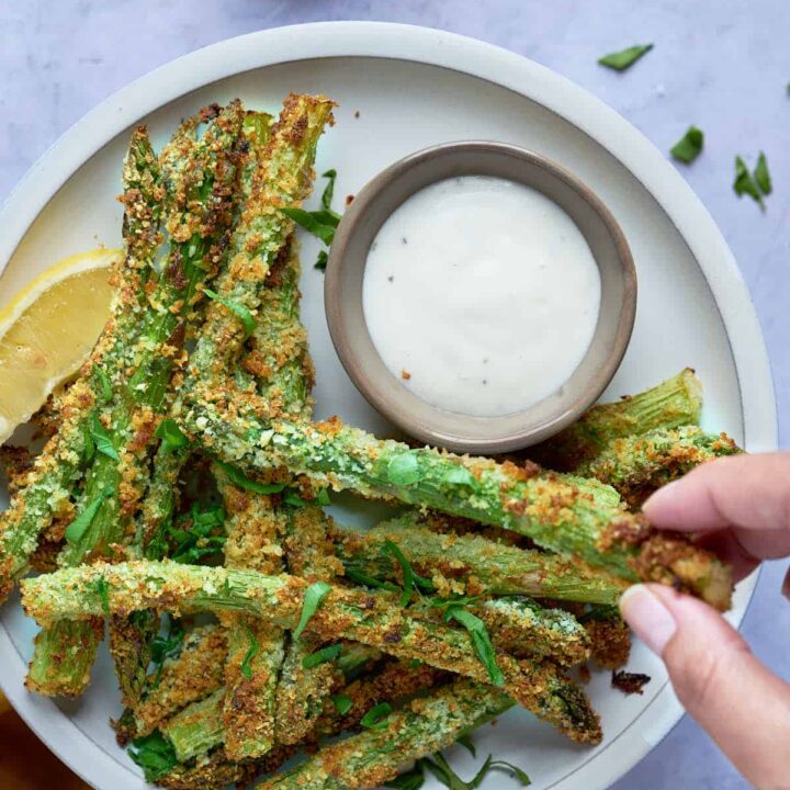 Asparagus fries made in the air fryer and served with dipping sauce and garnished with herbs.