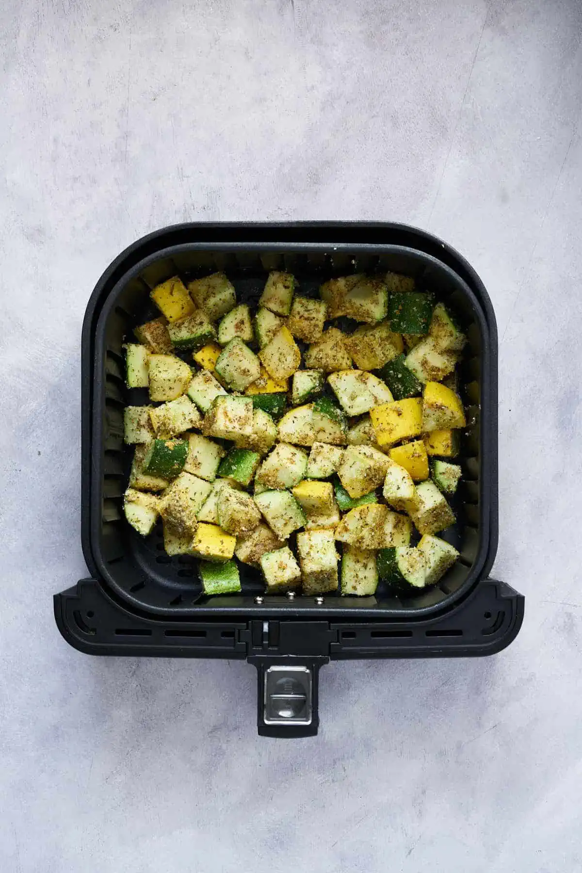 Seasoned yellow squash and zucchini in the air fryer basket before cooking.
