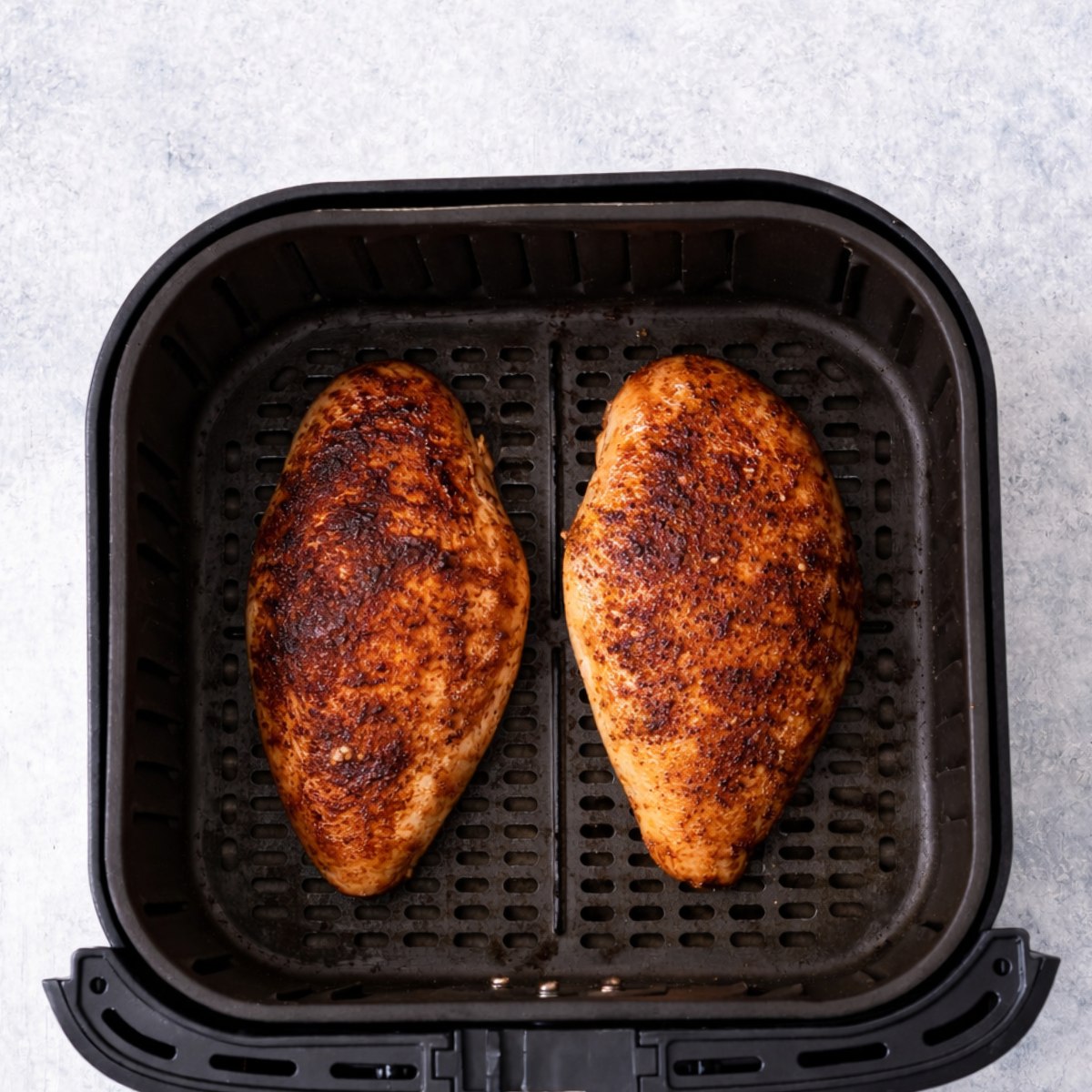 overcooked chicken breast in air fryer basket with dark browned surface