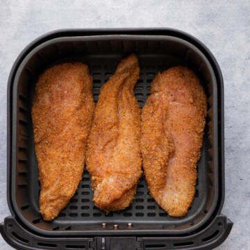 seasoned chicken breast with spices and oil in air fryer basket before cooking.