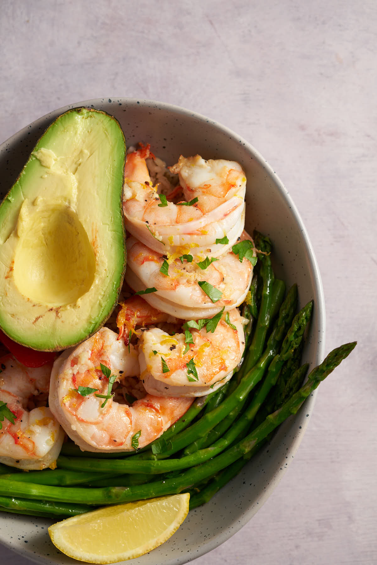 Lemon garlic shrimp bowl with brown rice, green beans, and fresh lemon in a ceramic bowl.
