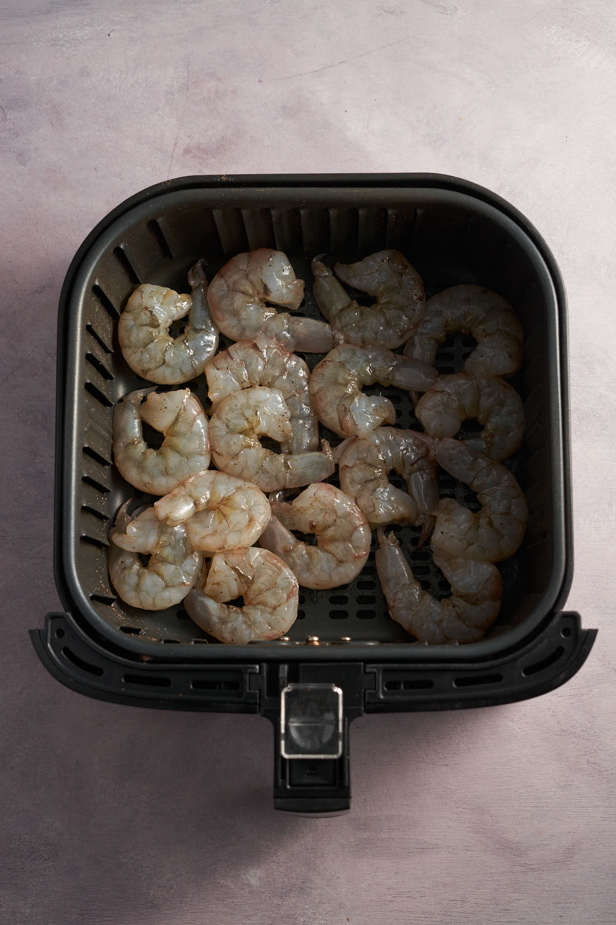 Seasoned raw shrimp arranged in a single layer in an air fryer basket.