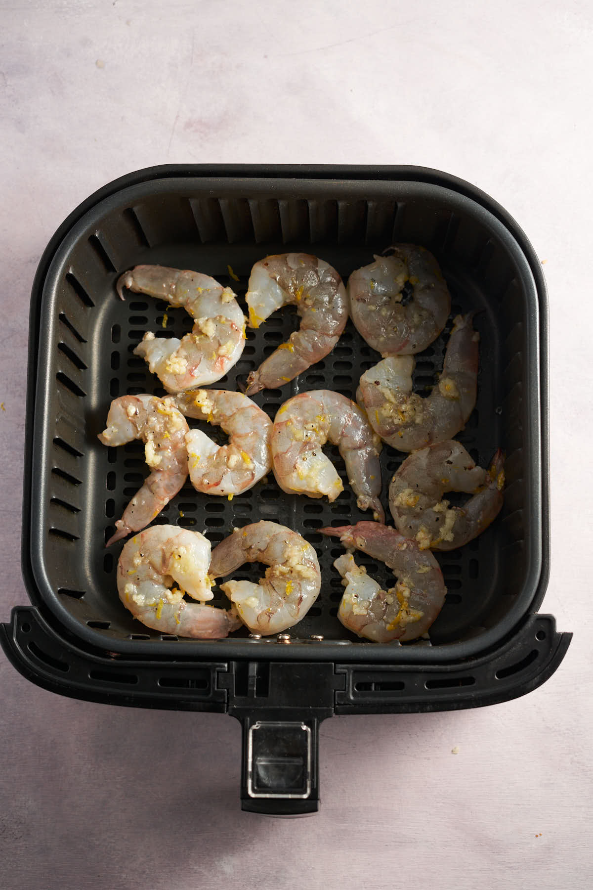 Seasoned lemon garlic shrimp arranged in a single layer in an air fryer basket