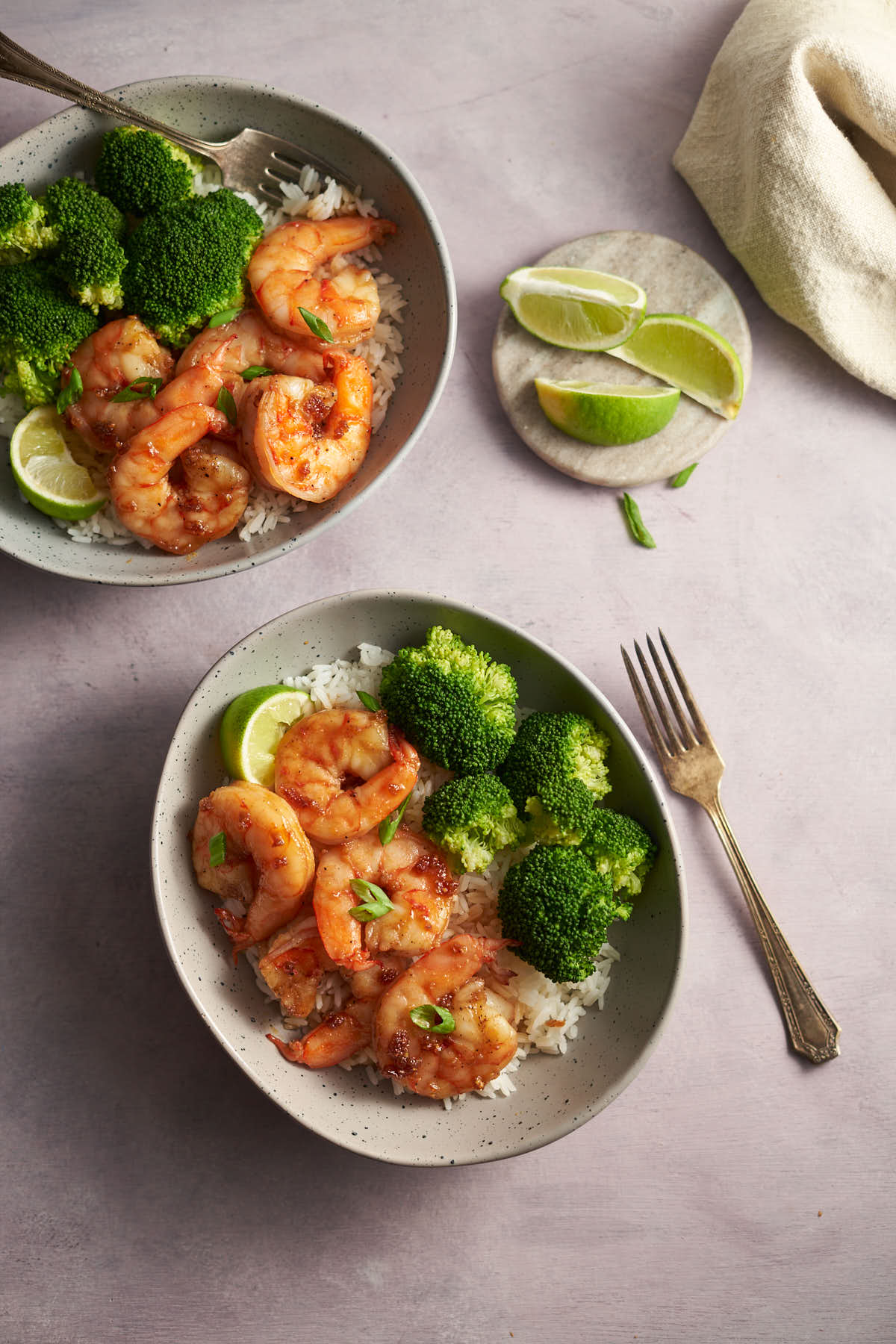 two honey garlic shrimp bowls with rice, broccoli and lime.