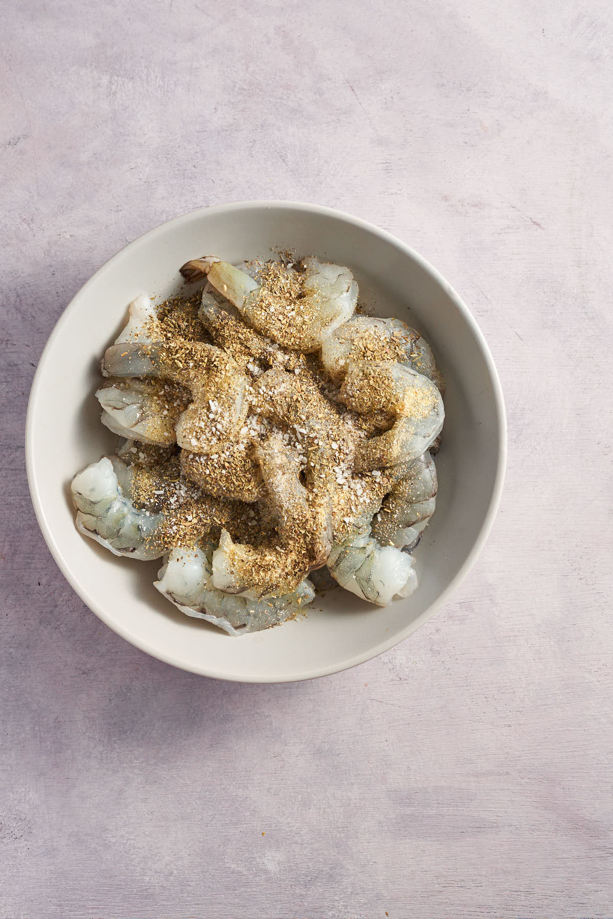 Raw shrimp coated with seasoning in a bowl.