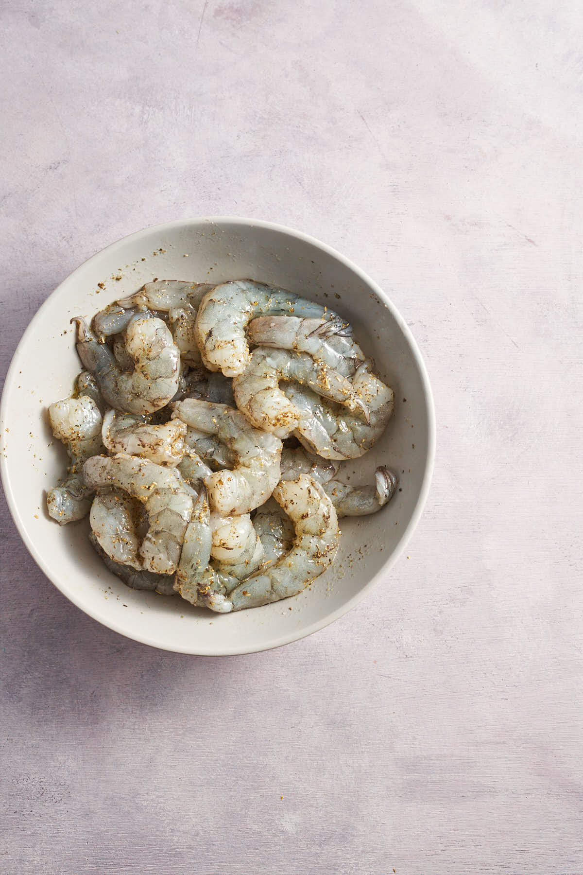 Seasoned raw shrimp in a bowl before cooking.