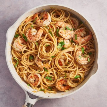 Overhead view of lemon garlic shrimp pasta in a skillet with parsley and lemon zest