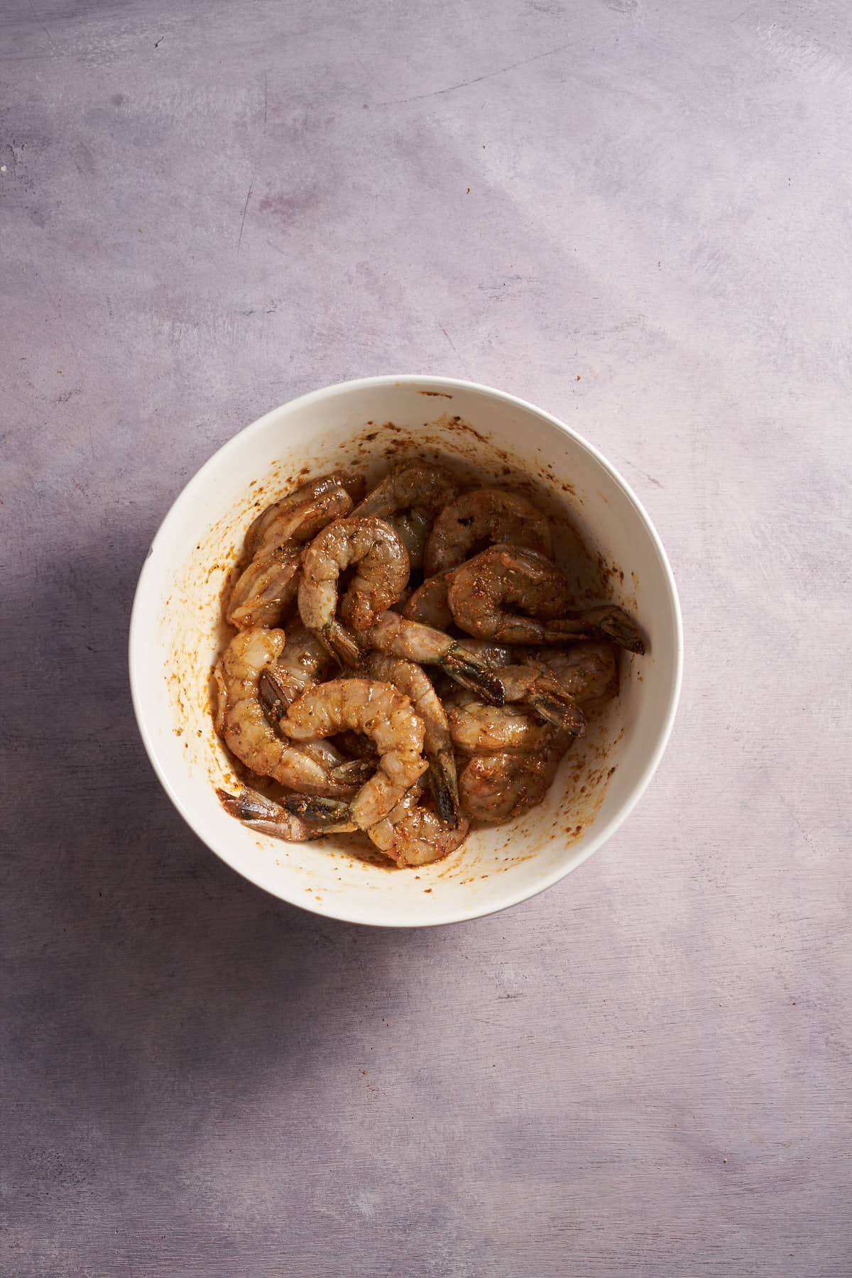 Raw shrimp coated with seasoning in a mixing bowl.