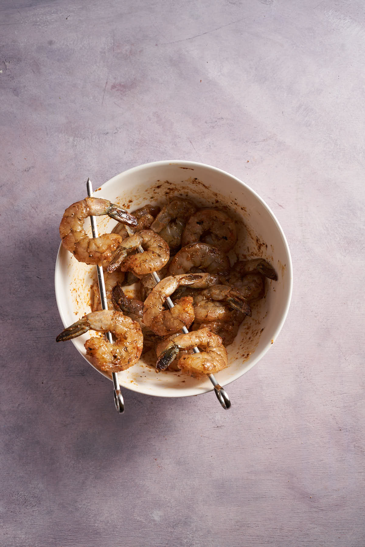 Seasoned raw shrimp threaded onto skewers before air frying.