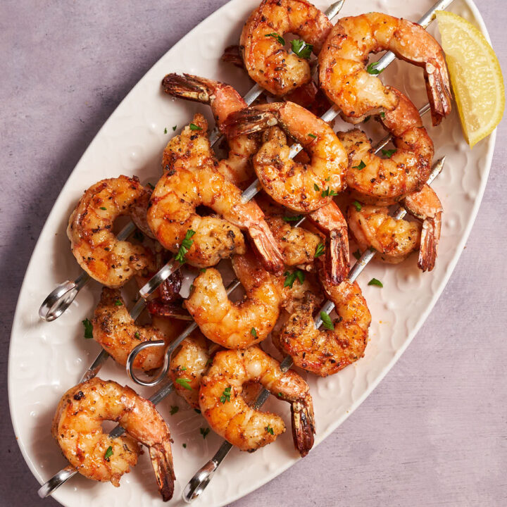 Air fryer shrimp skewers arranged on a white platter with lemon wedges.