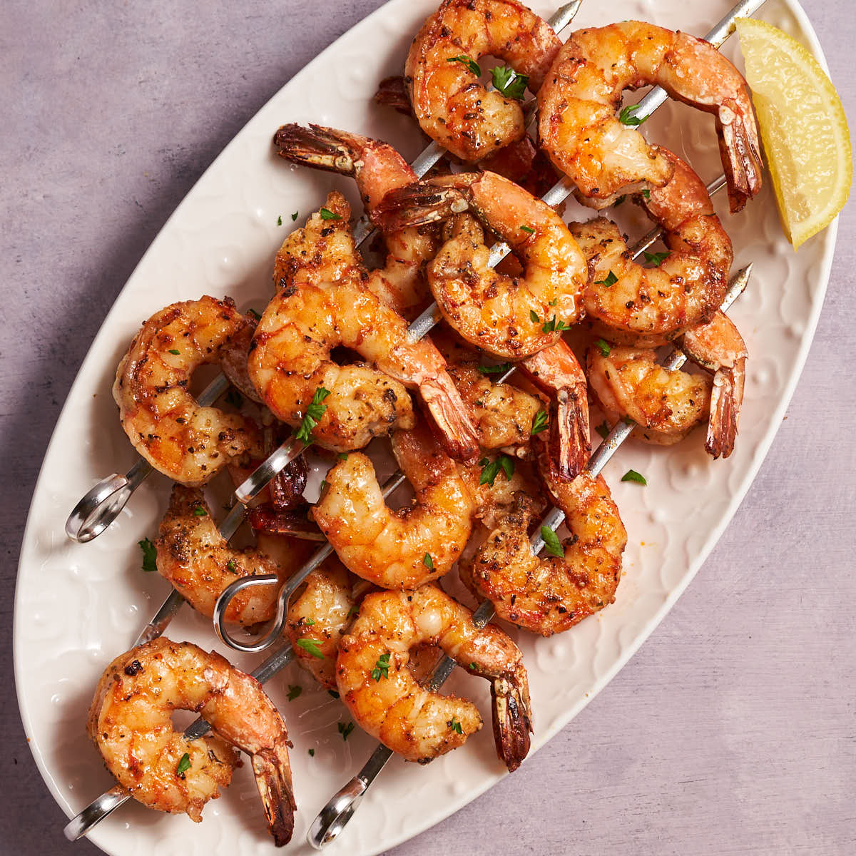 Air fryer shrimp skewers arranged on a white platter with lemon wedges.