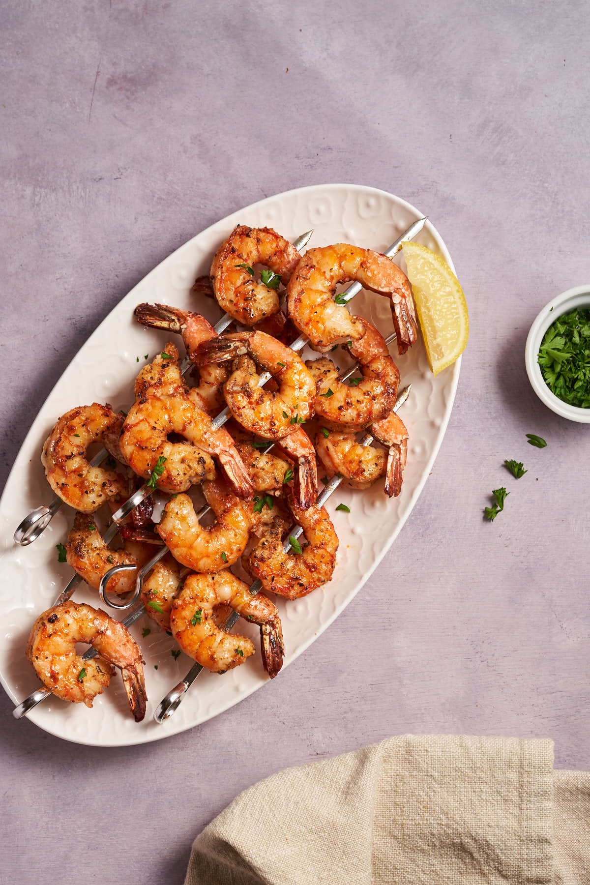 shrimp skewers arranged on a white platter with lemon wedges.