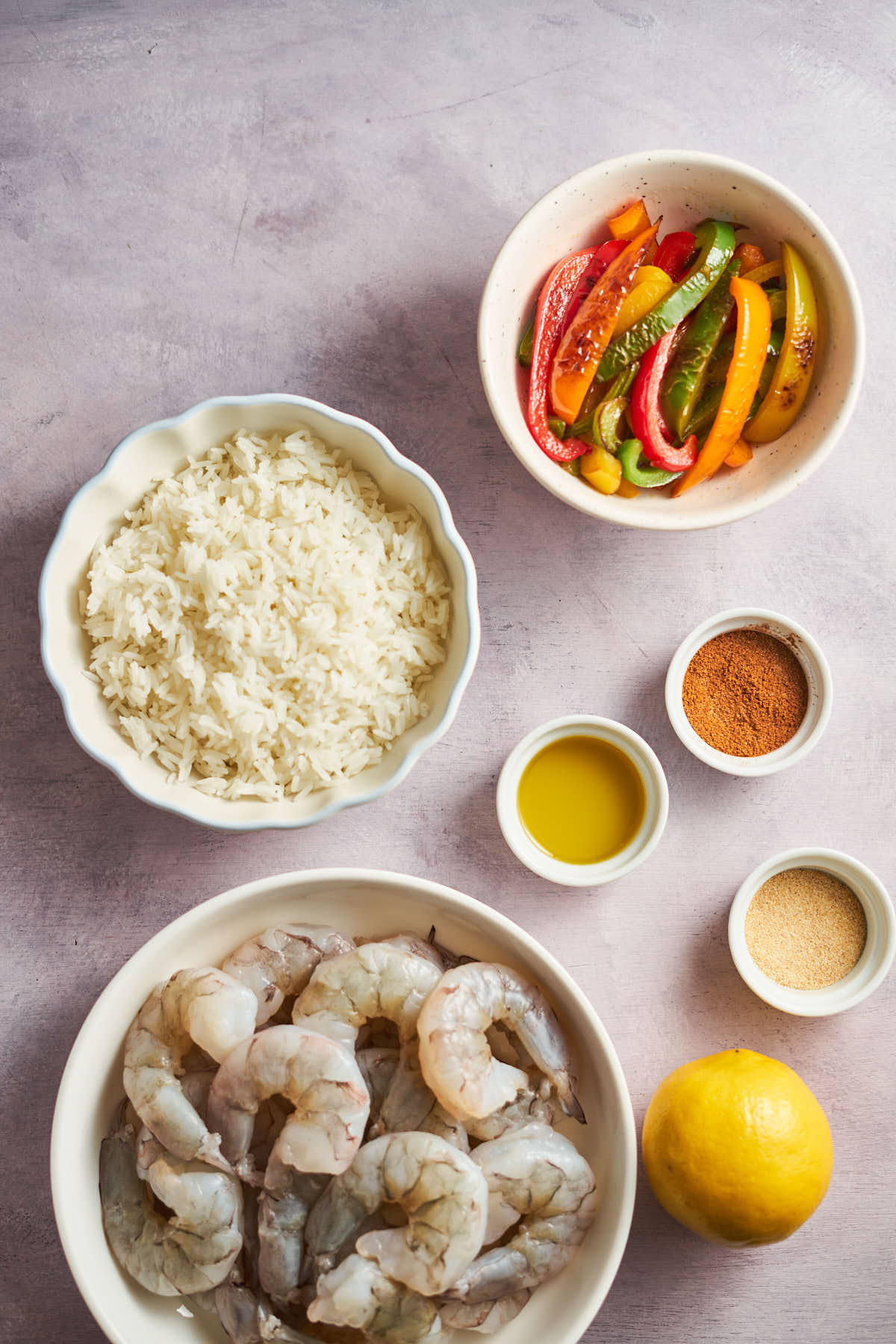 Raw shrimp, cooked rice, bell peppers, Cajun seasoning, oil, garlic powder, and lemon for Cajun shrimp bowls.