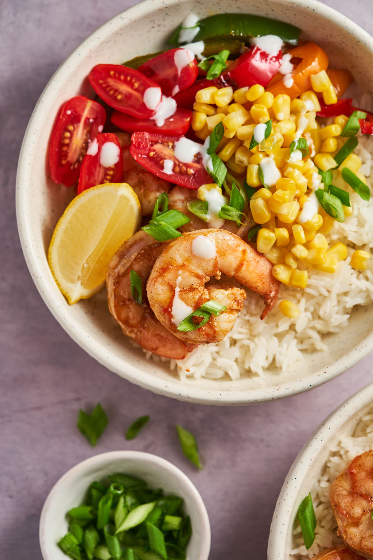 Overhead close-up of Cajun shrimp with rice, corn, cherry tomatoes, and lemon in a bowl.