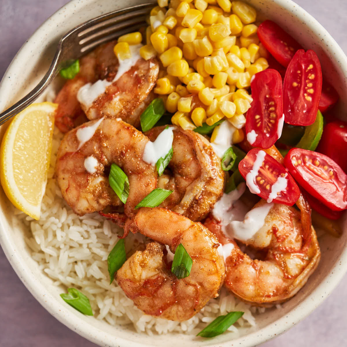 Close-up of a Cajun shrimp bowl with rice, corn, cherry tomatoes, and a creamy drizzle.