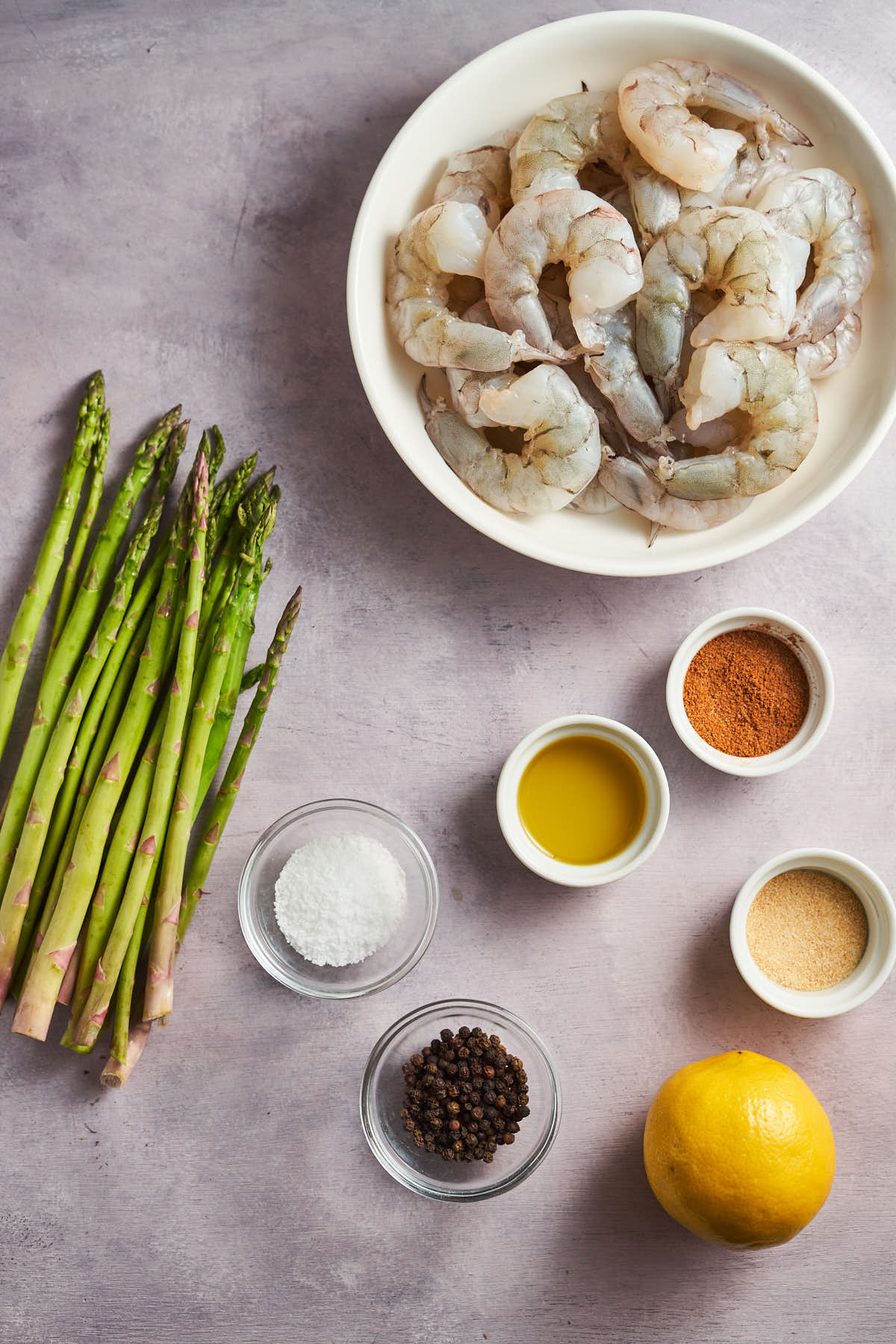 Raw shrimp, asparagus, Cajun seasoning, oil, garlic powder, salt, pepper, and lemon for Cajun shrimp sheet pan dinner.