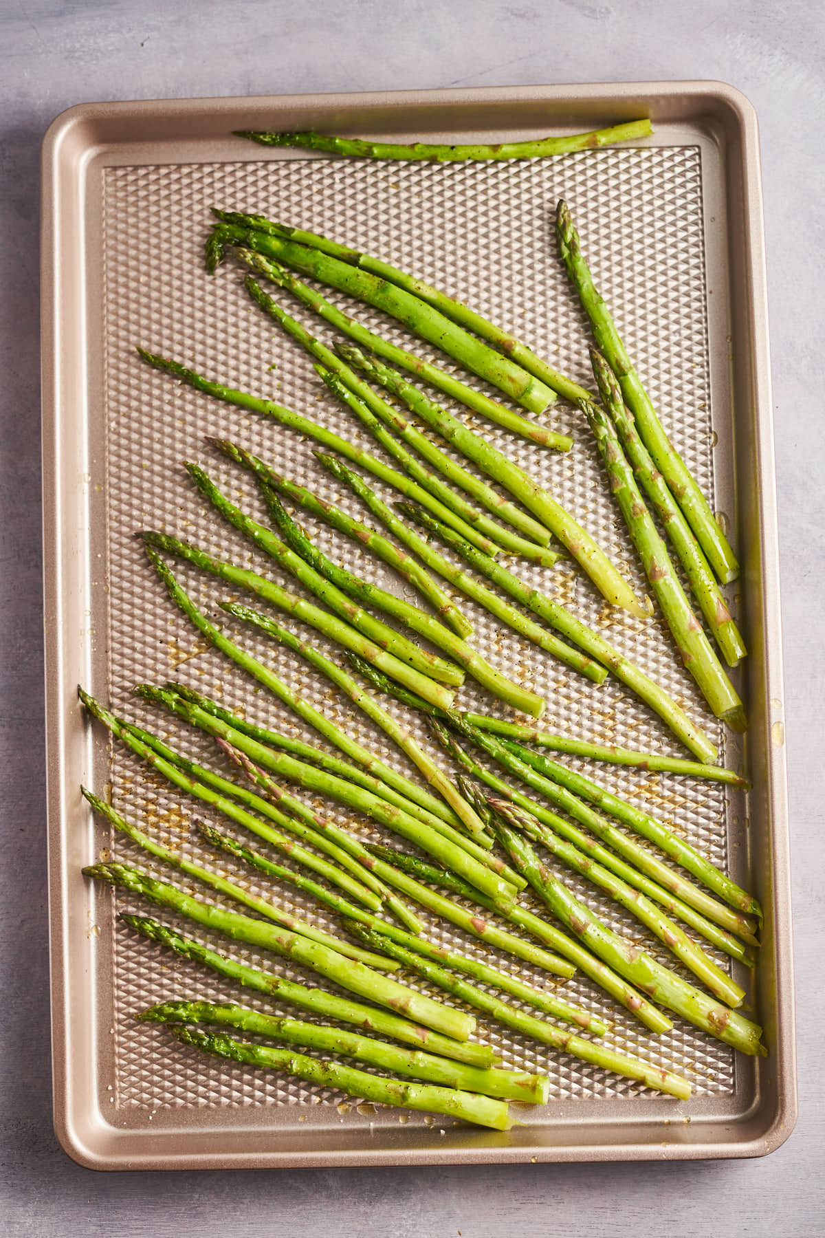 Asparagus spears spread in a single layer on a sheet pan.