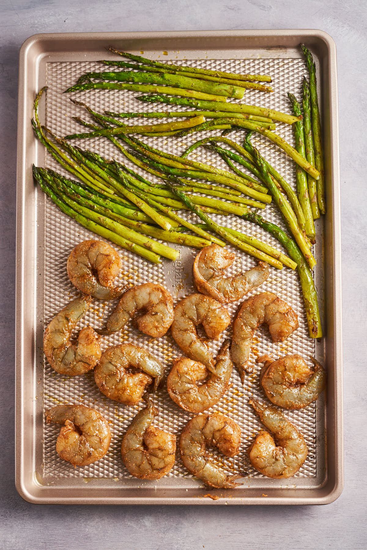 Cajun seasoned shrimp arranged beside asparagus on a sheet pan.