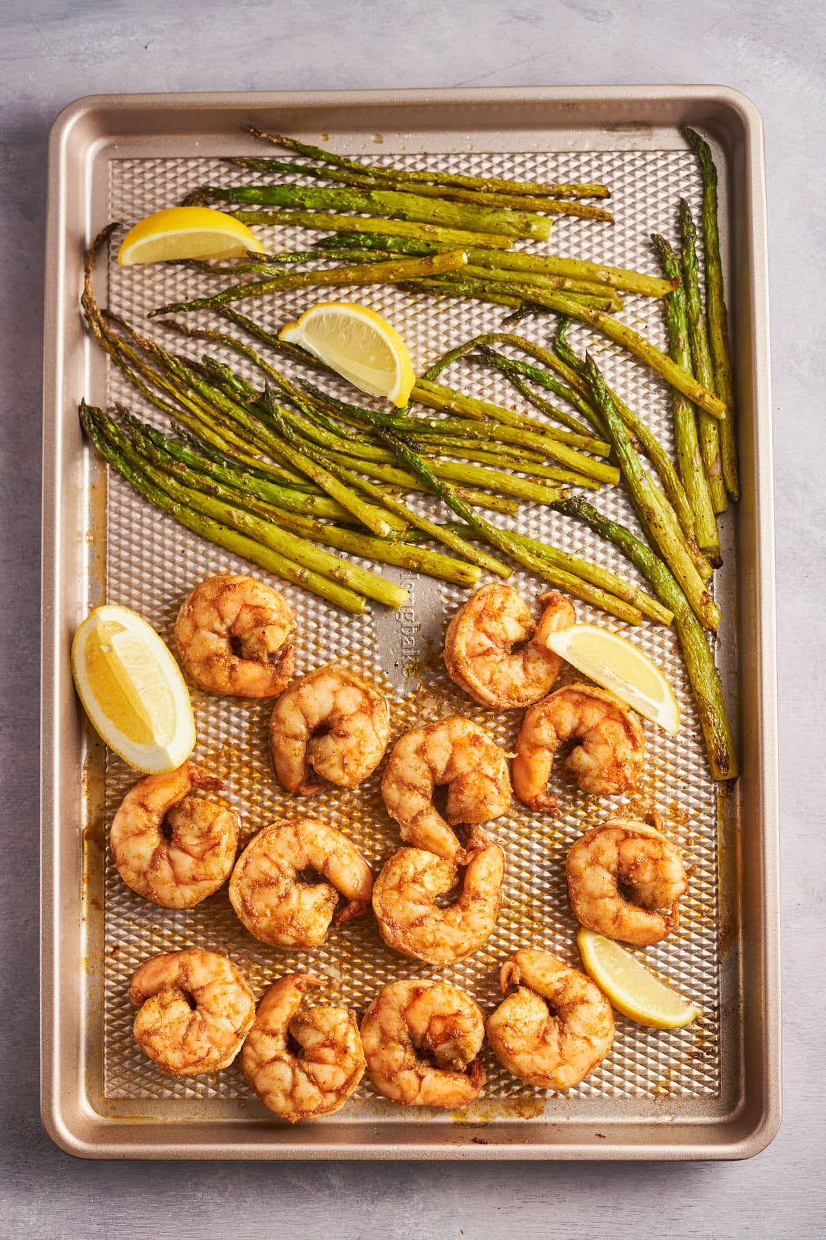 Cajun shrimp and roasted asparagus on a sheet pan with lemon wedges.